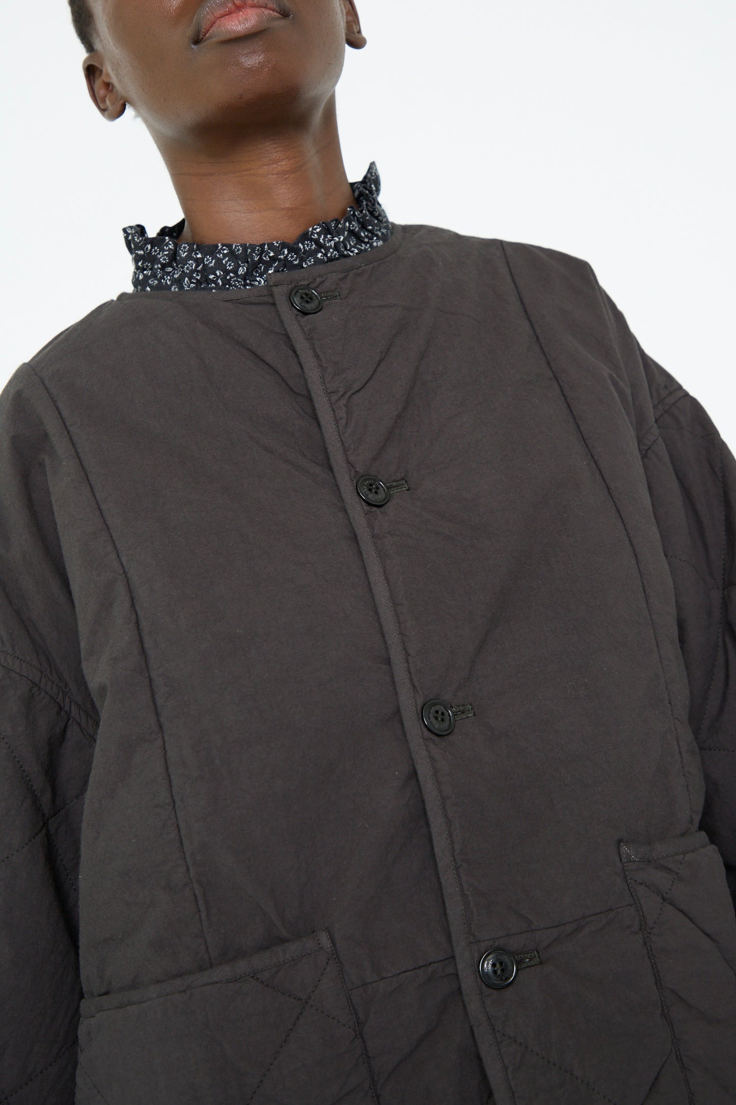 A close up of a woman's neckline, wearing the nest Robe's UpcycleLino Reversible Quilted Coat in Ink Black. 