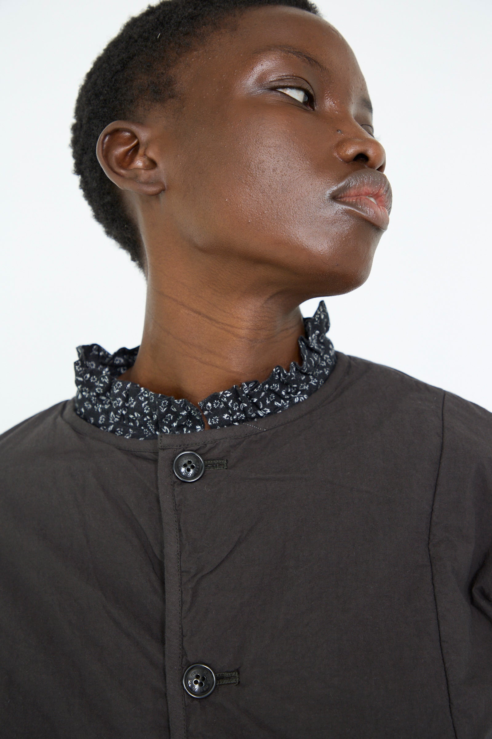 A woman wearing the UpcycleLino Reversible Quilted Coat in Ink Black by nest Robe looks to the side against a plain background.