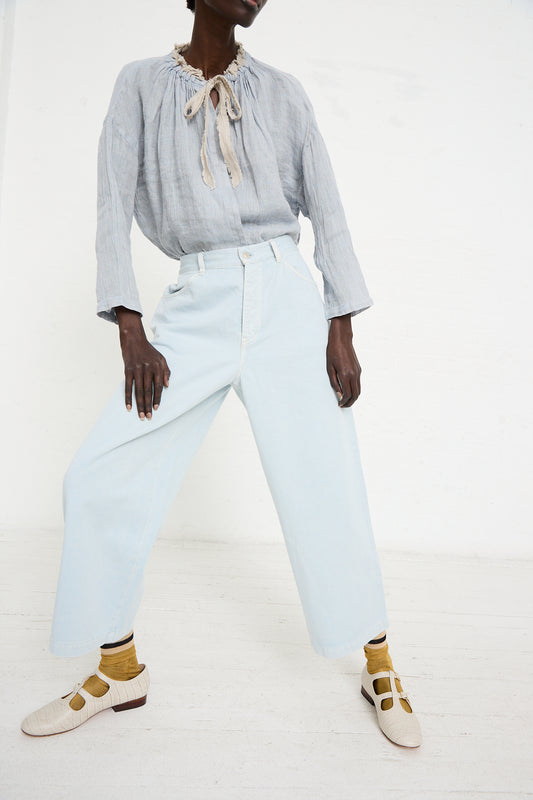 Person wearing a light grey blouse with a ruffled collar and tie, UpcycleLino Chino Wash-Colored Pant in Light Blue by nest Robe, mustard socks, and beige shoes with brown detailing, posed against a white background.