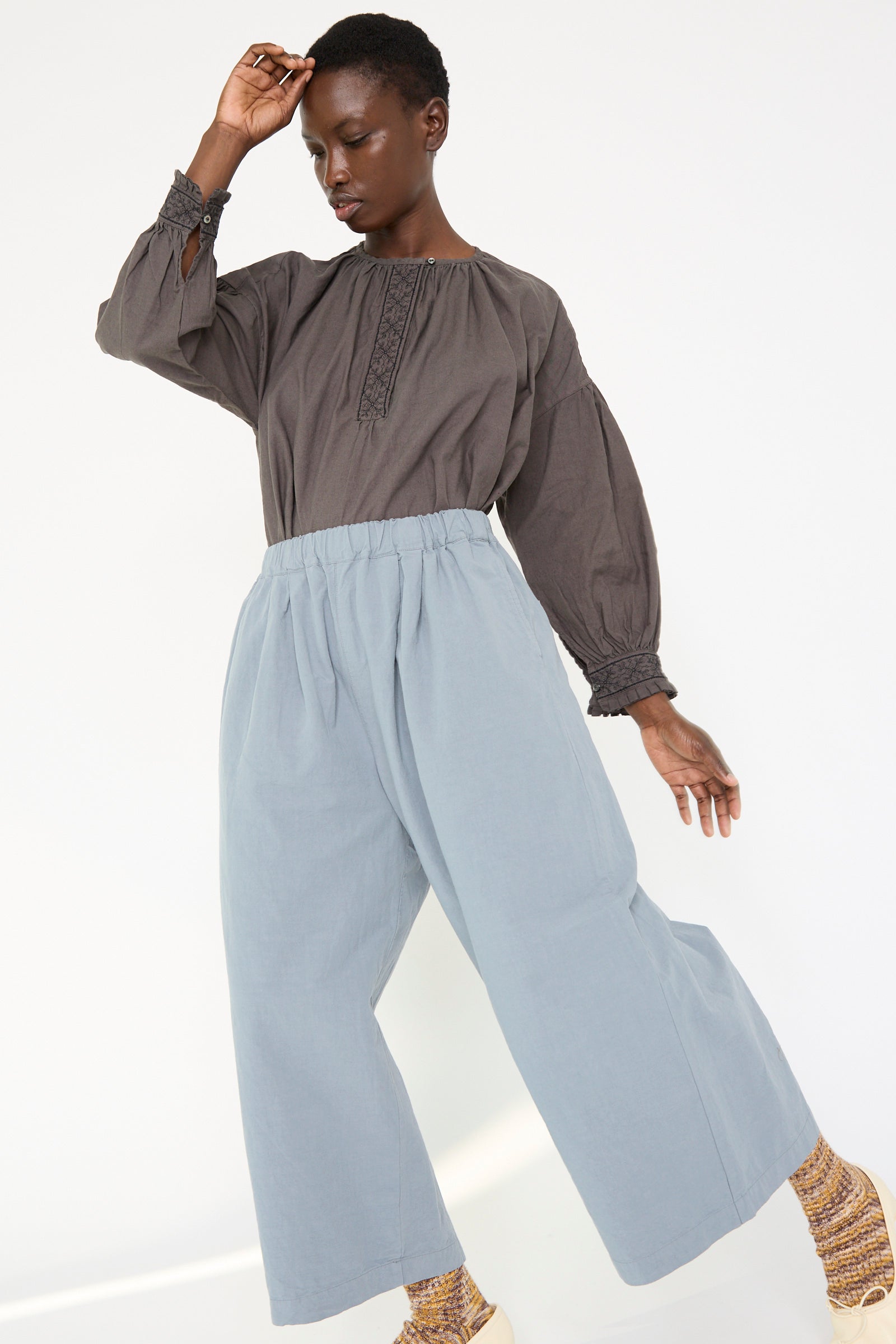 A woman wearing a dark long-sleeve top and the Water Repellent Cotton Linen Omi-Zarahi Wide Pant in Blue from nest Robe poses against a plain background with her arm raised.