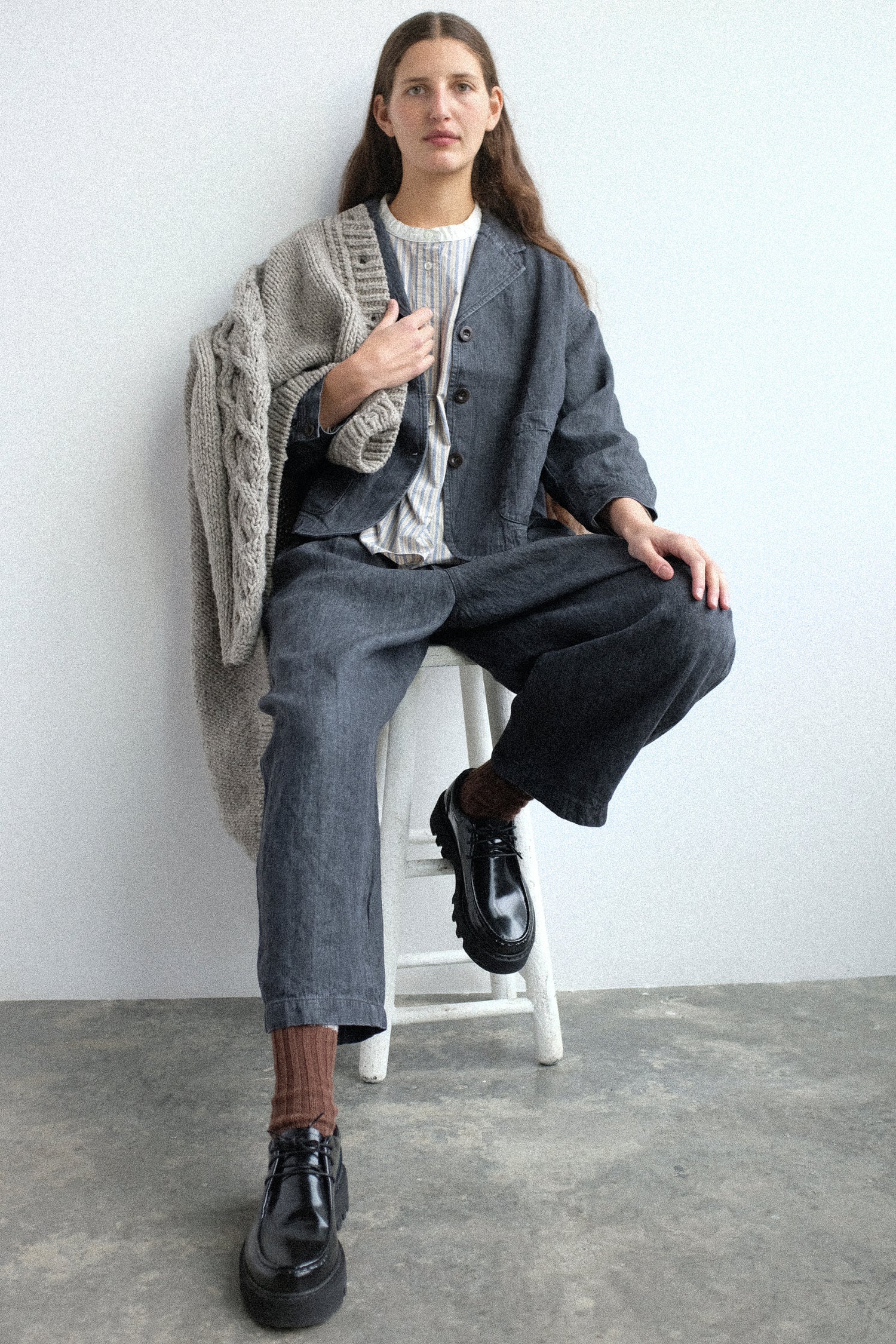 Woman sitting on a stool wearing pieces from nest Robe's FW25 collection with a white background
