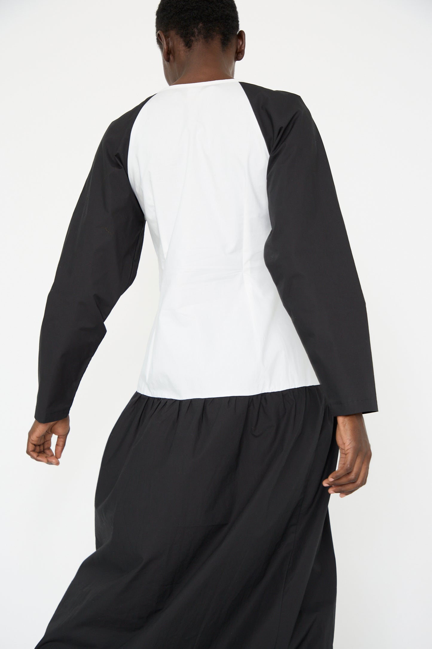 A woman is seen from behind, dressed in the SC103 Cotton Poplin Frame Dress in Flash, featuring a relaxed fit with long sleeves and a flowing skirt, all set against a plain background.