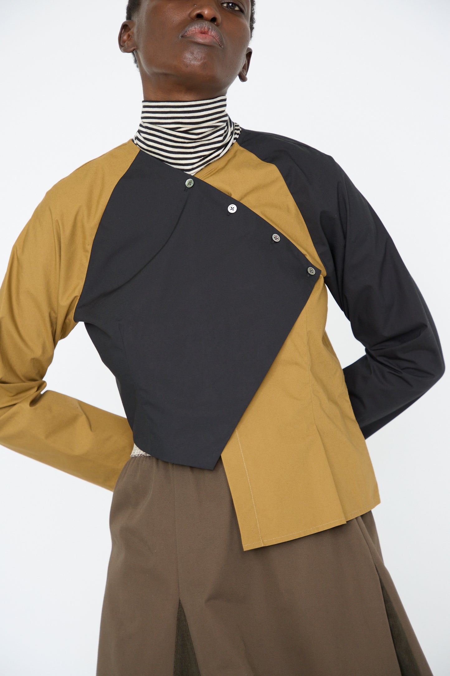 A woman dressed in a Cotton Poplin Peak Blouse in Oblique from SC103, paired with a striped turtleneck underneath.