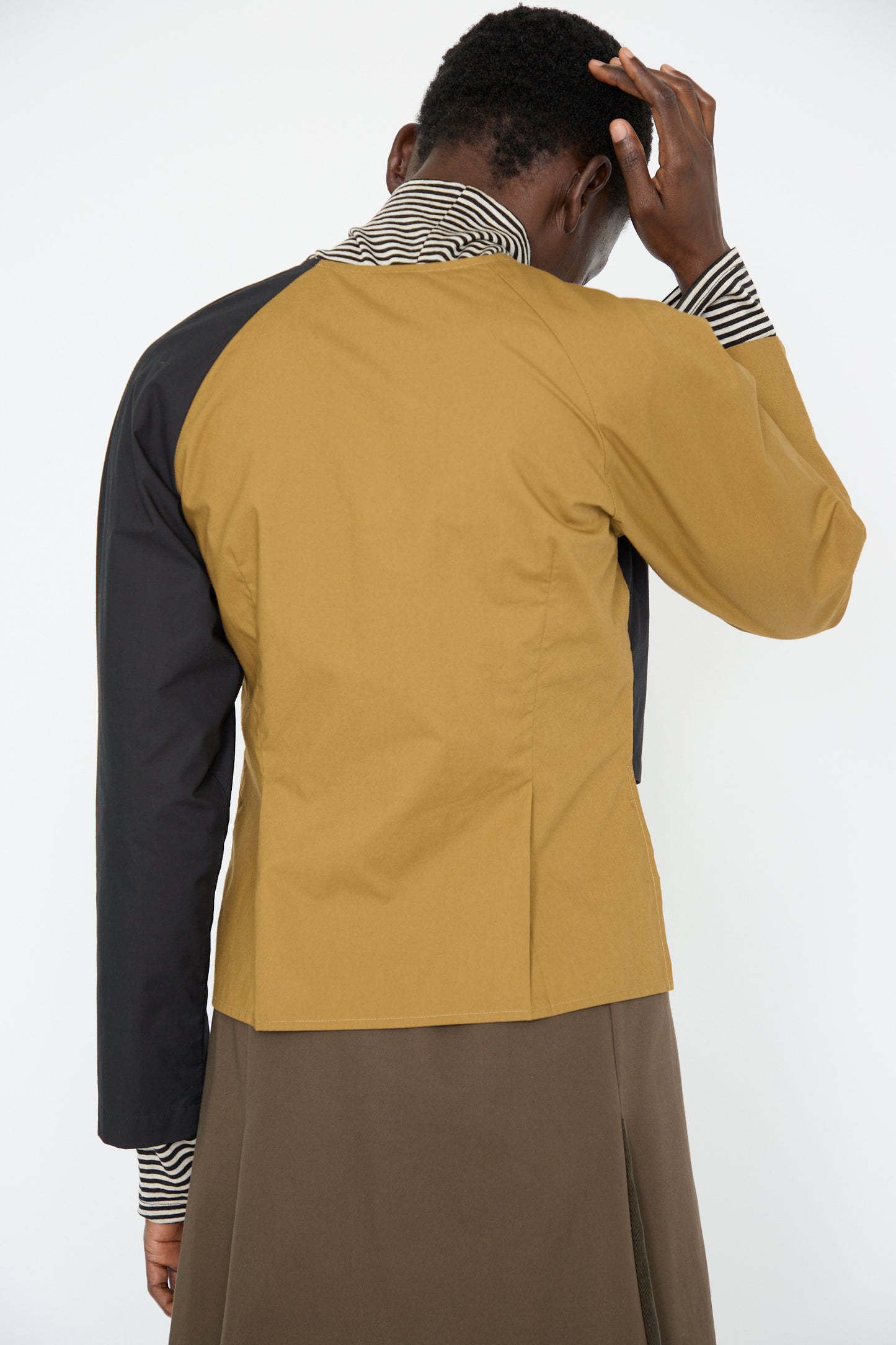 A woman wearing the SC103 Cotton Poplin Peak Blouse in Oblique is seen from behind with her hand on the back of her head. 