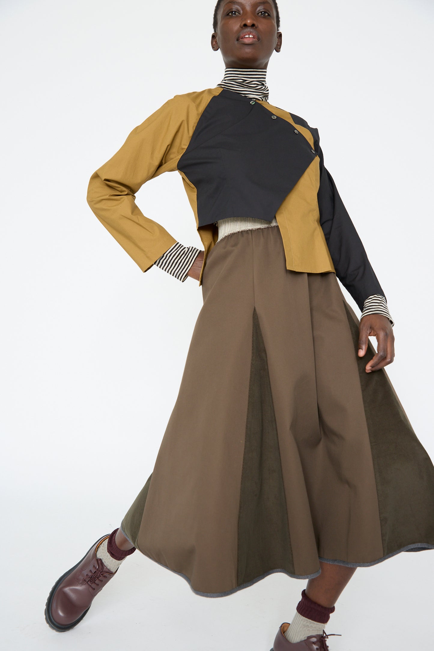 A woman wears the Cotton Twill Axis Skirt in Beam by SC103, with brown boots and socks.