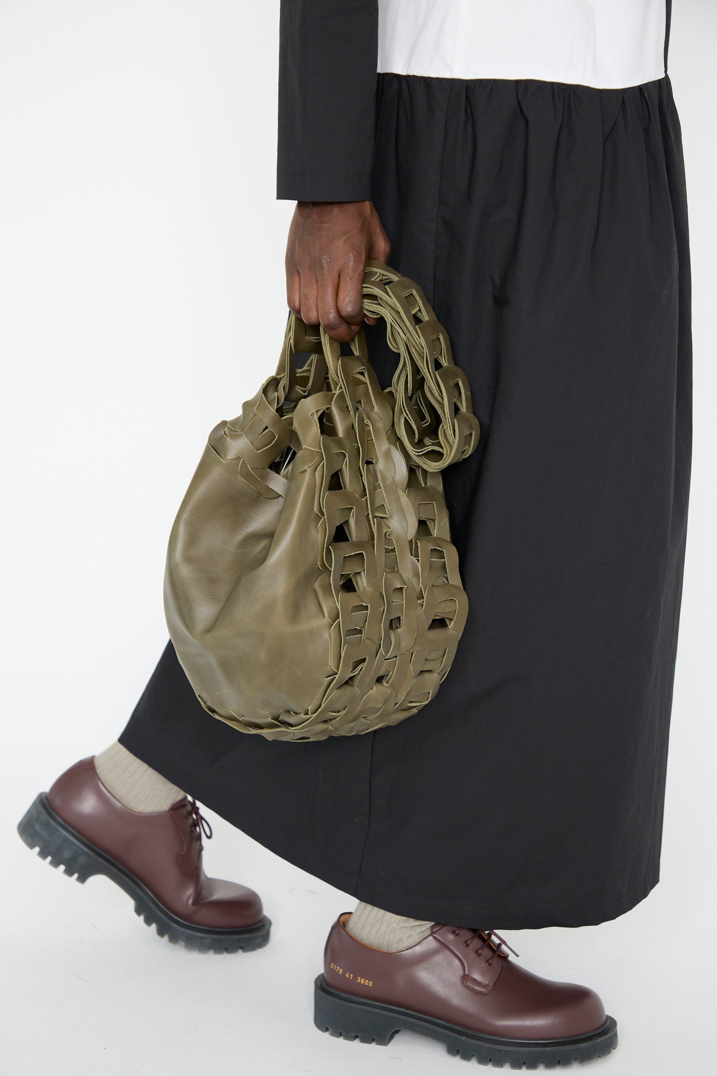 A person in a long black skirt and dark brown shoes carrying an SC103 Leather Drum Bag in Olive.