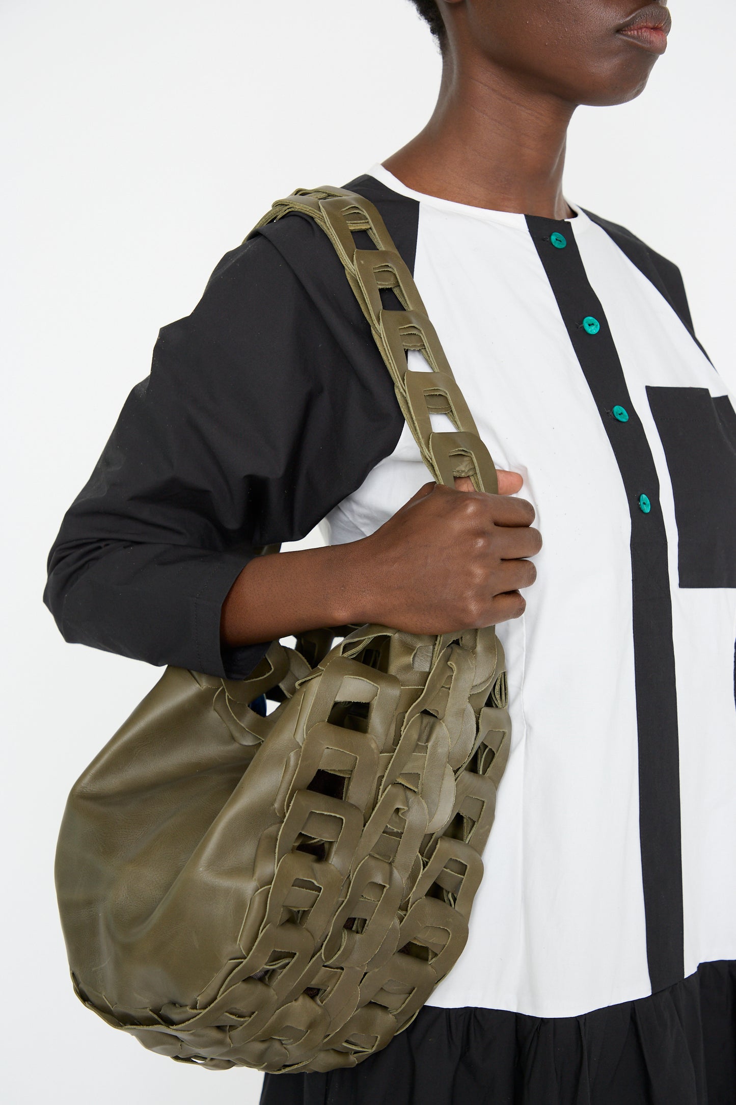 A person is holding a Leather Drum Bag in Olive by SC103, wearing a black and white dress with green buttons.