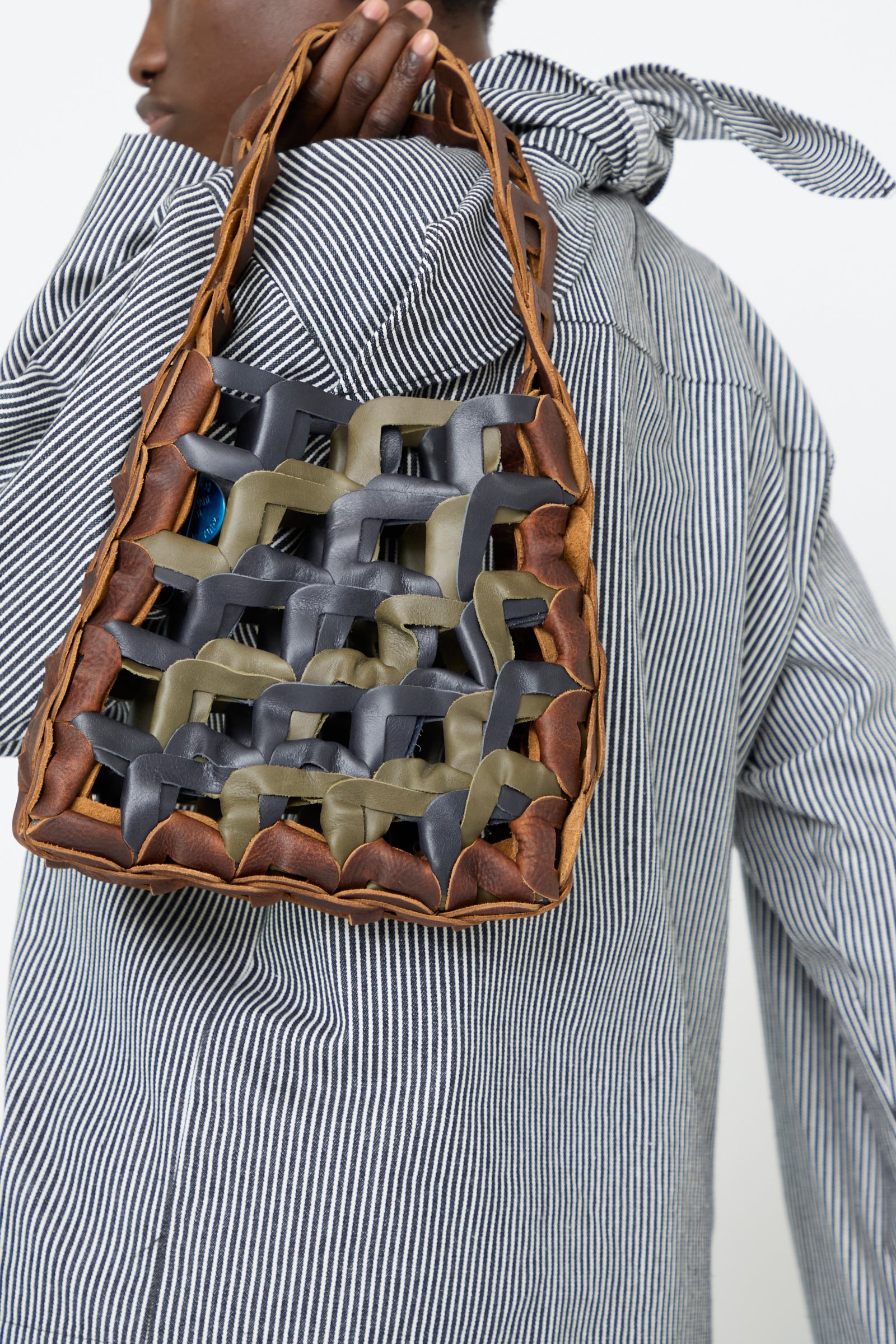 A woman wearing a striped shirt holding the Leather Links Tote in Anise with Green by SC103, featuring an interlocking leather design against a white background.