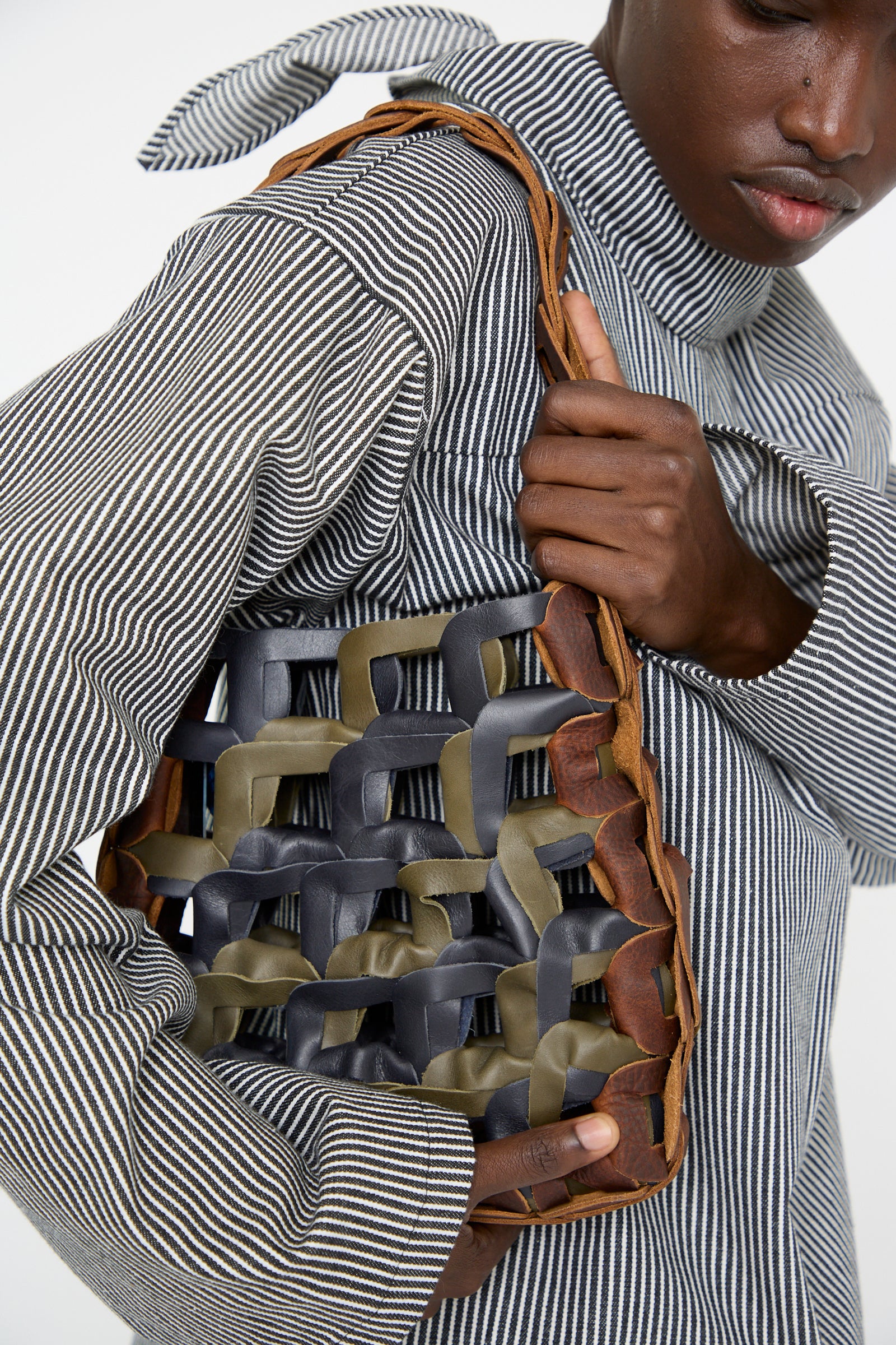 A woman is holding the SC103 Leather Links Tote in Anise with Green, dressed in a striped outfit and looking down against a white background.