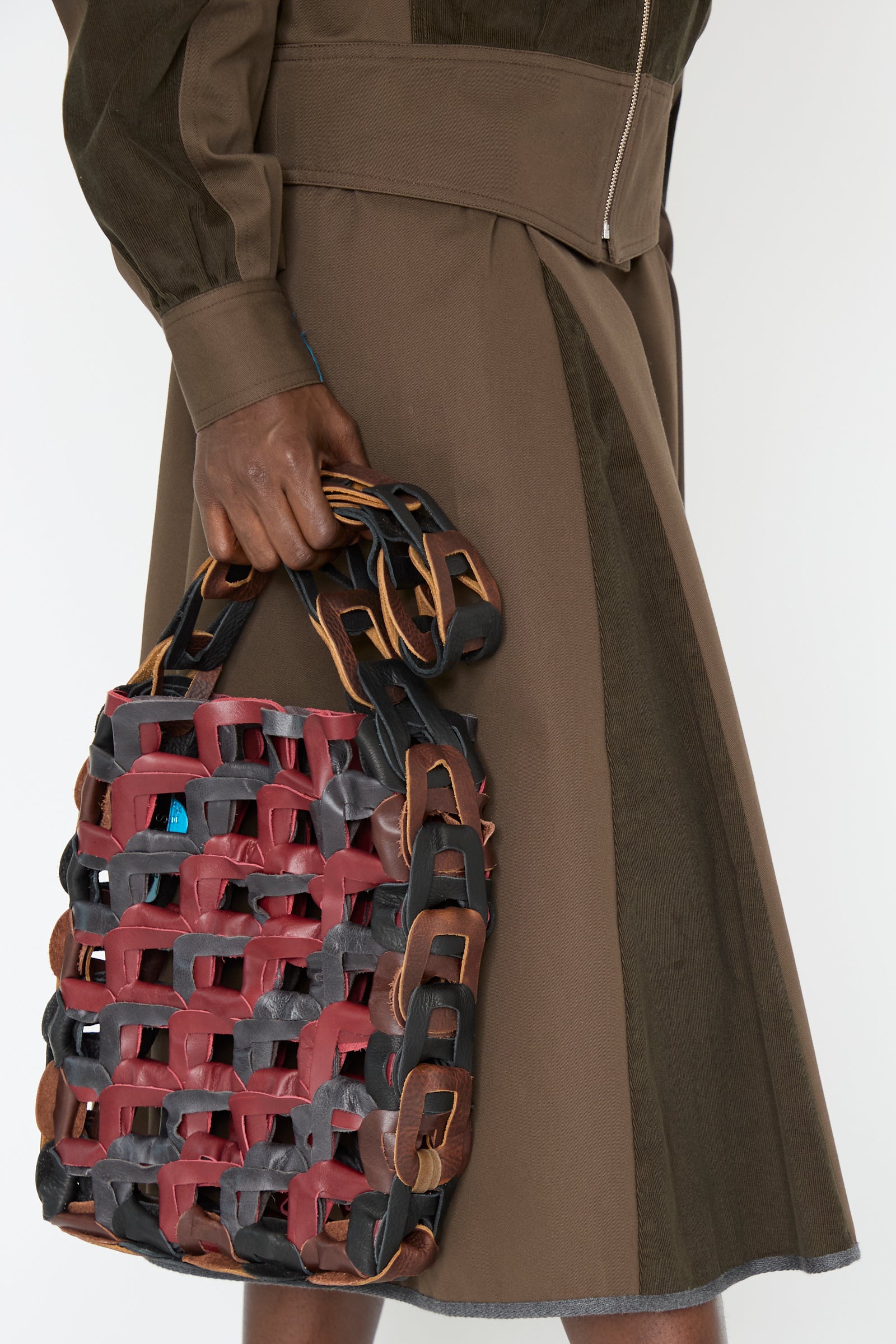 A person carries the Leather Medium Links Tote in Cinema by SC103, with an olive green and brown top and skirt set.