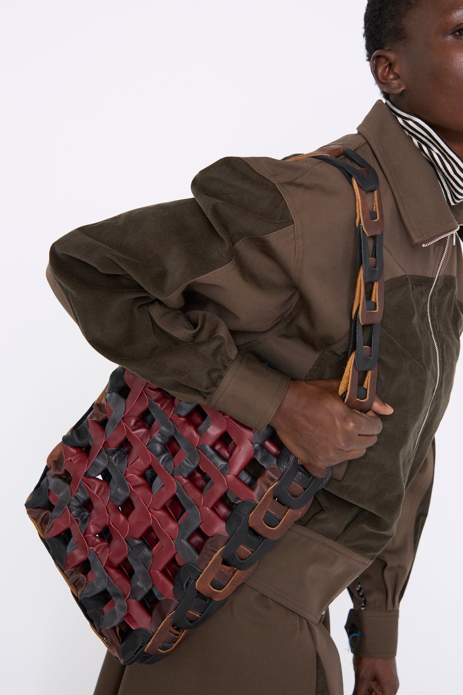 A person dressed in a brown outfit carries the Leather Medium Links Tote in Cinema by SC103, which features a thick strap, against a white background.