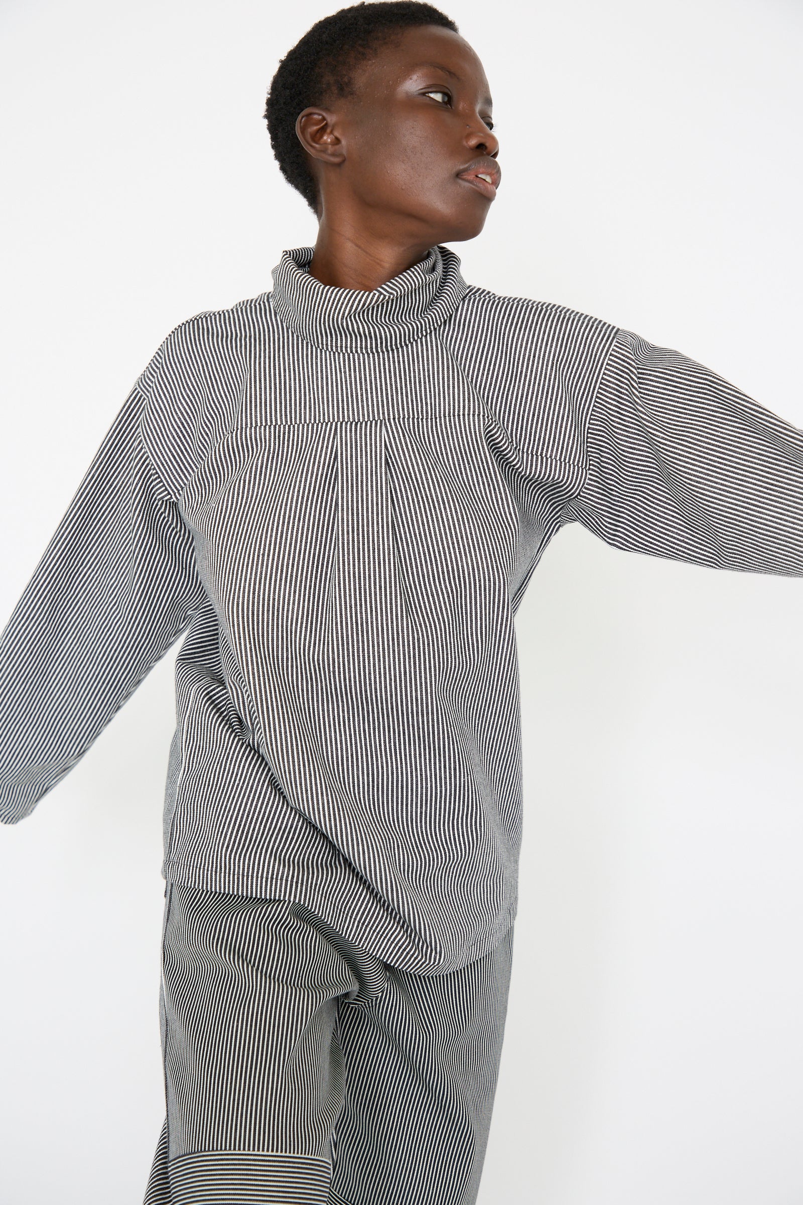 A woman dressed in the Stripe Denim Compass Blouse in Railroad by SC103 gazes to the side, set against a plain background.