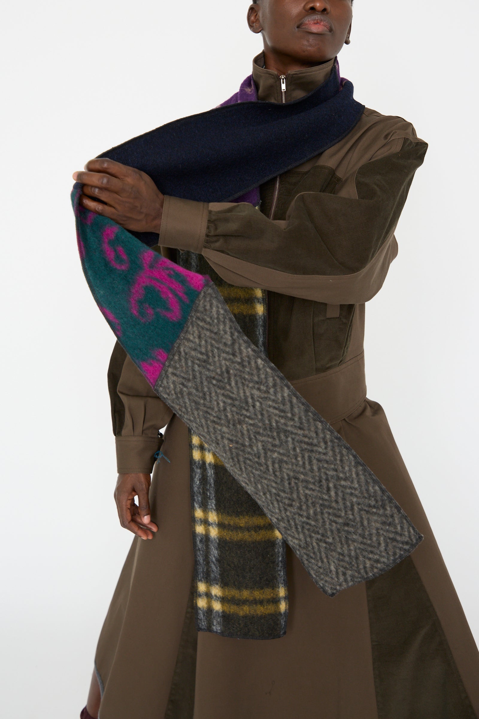 A woman in a brown coat holds the Wool Mix Ladder Scarf in Attic by SC103, showcasing pattern block artistry that merges herringbone, plaid, and abstract designs.