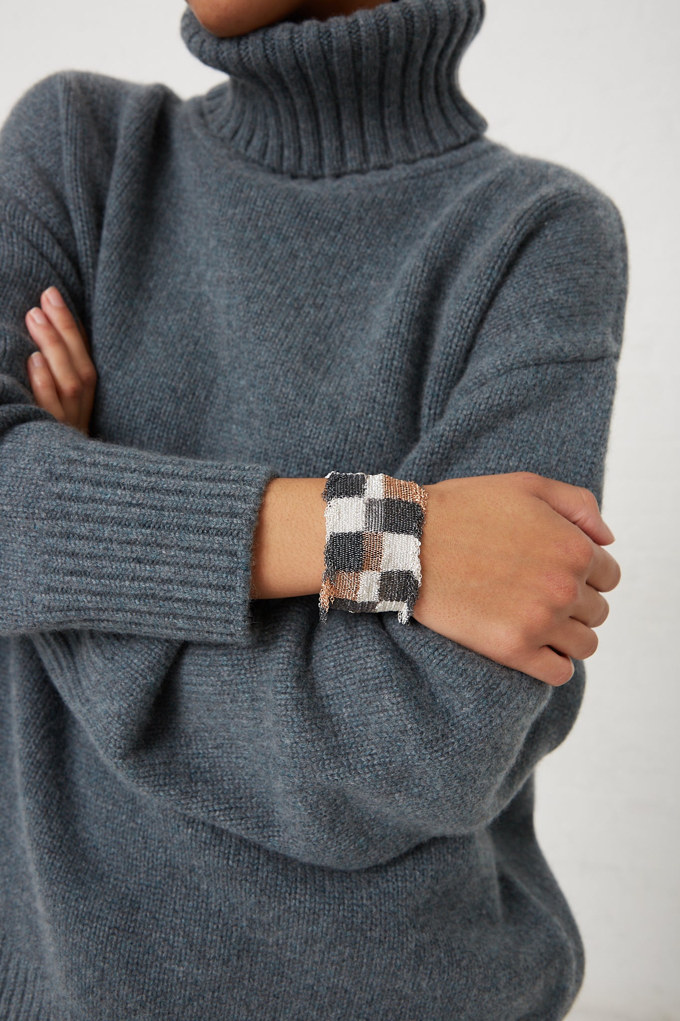 A woman wearing a grey sweater with a checkered cuff and a Stephanie Schneider Rose Gold Plated and Silk Silver Bracelet.
