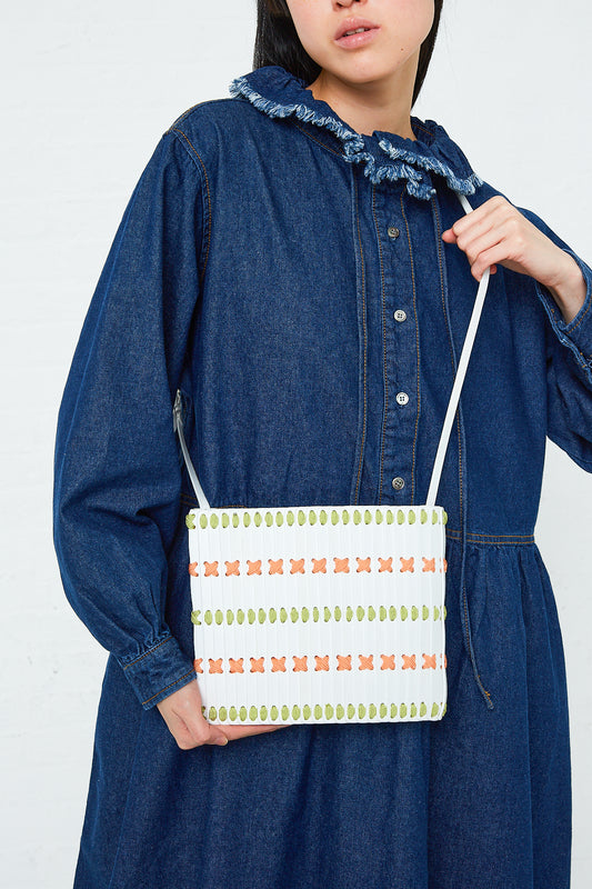 A woman in a denim dress holding a Hatori Crossbody Bag 46 in Bianco, Lime and Pink.