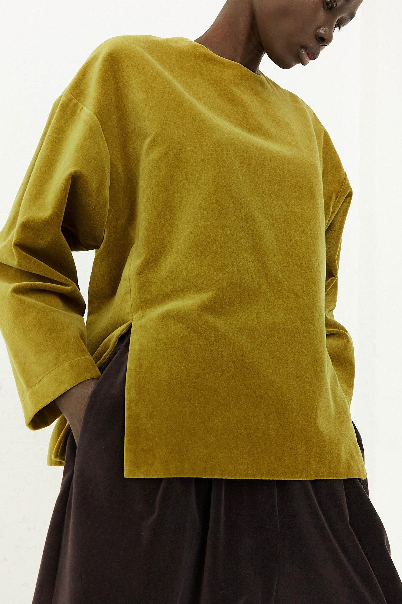 A model wearing a yellow Black Crane Cotton Velveteen Slit Top with a relaxed fit.