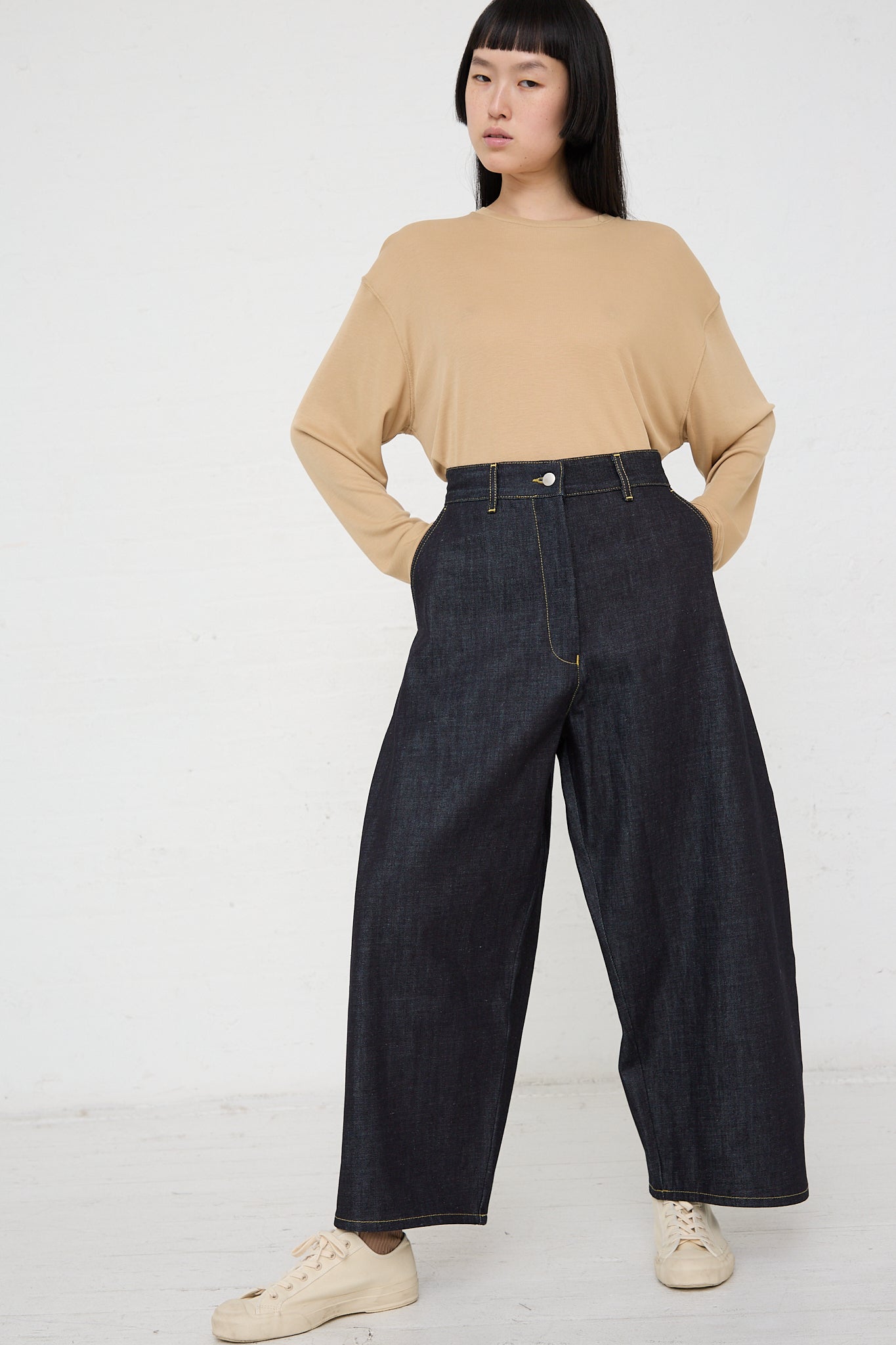 A woman wearing a beige tee and Studio Nicholson's Chalco Wide Crop Jean in Raw Indigo wide leg pants in an oversized fit.