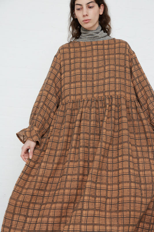 A woman wearing an Ichi Antiquités Woven Wool Check Dress in Terracotta with a wide neck in a brown checkered pattern.