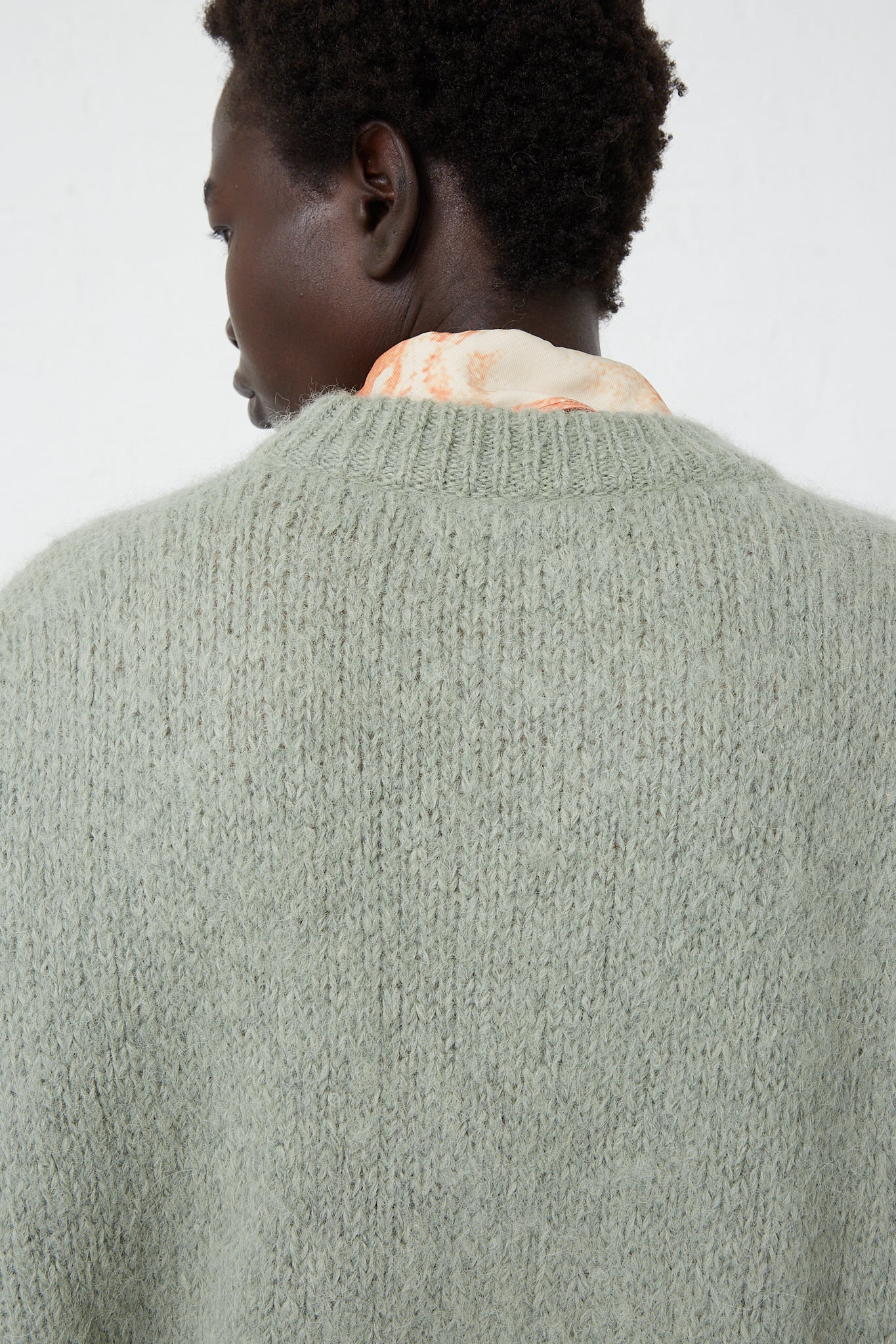 The back view of a woman wearing a green Rejina Pyo Alpaca Blend Toni Sweater in Mint with crew neck and logo detail.