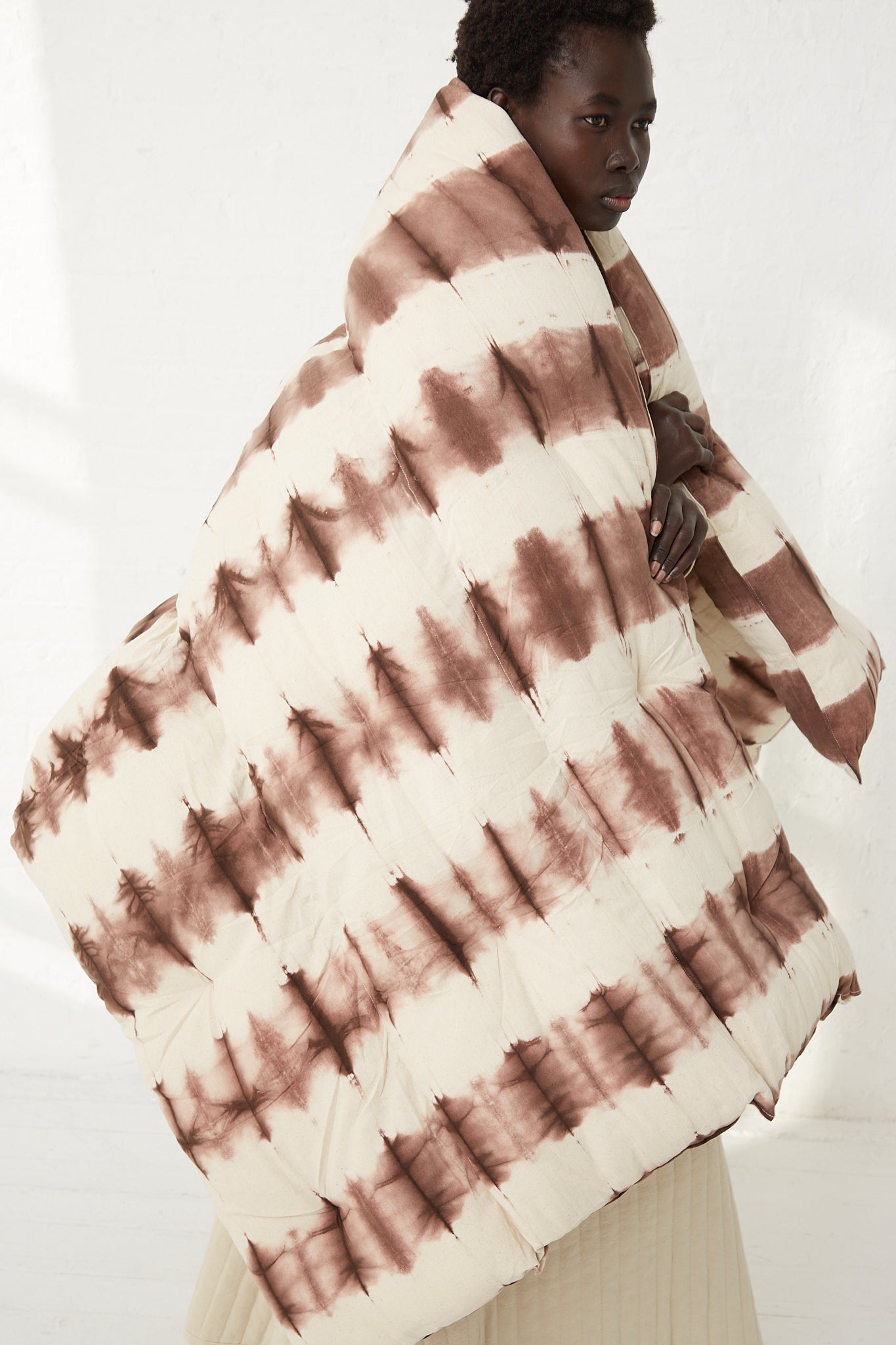 A woman wearing a Tensira hand-dyed cotton Tufted Overlay Mattress in Chocolate Tie Dye blanket.