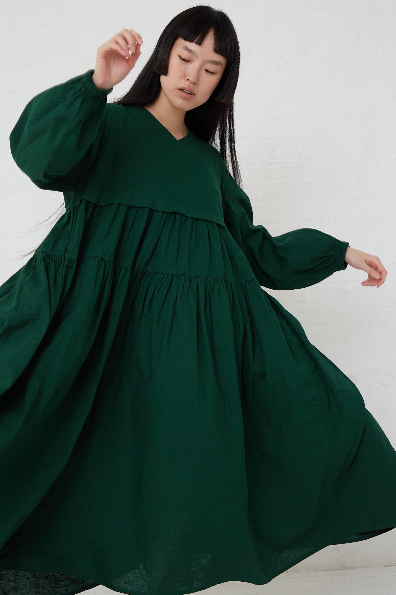 A woman is wearing the UpcycleLino Linen Tiered Gather Dress in Green by nest Robe.
