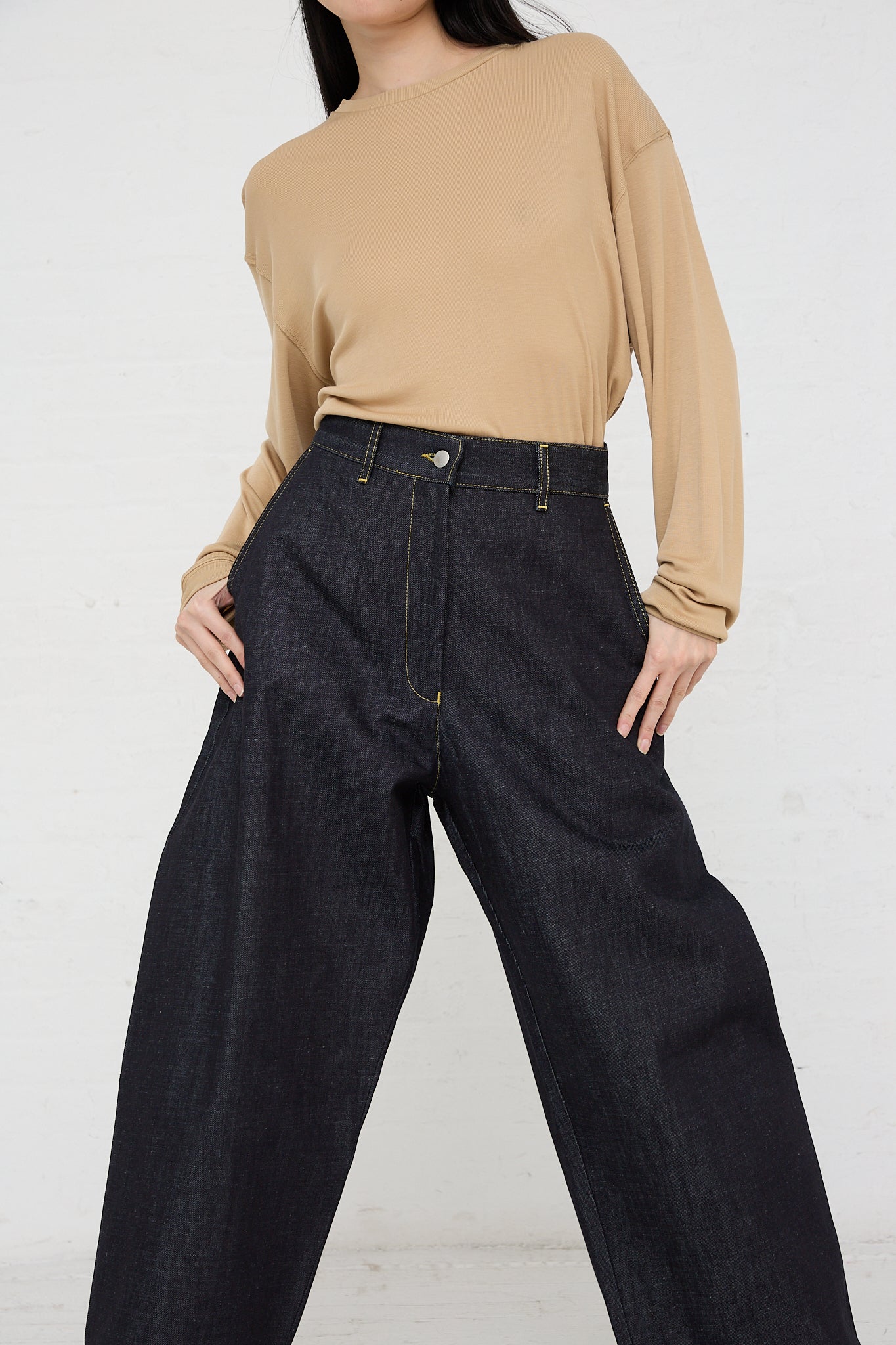 The model is wearing a beige tee and Studio Nicholson's Chalco Wide Crop Jean in Raw Indigo with an oversized fit.