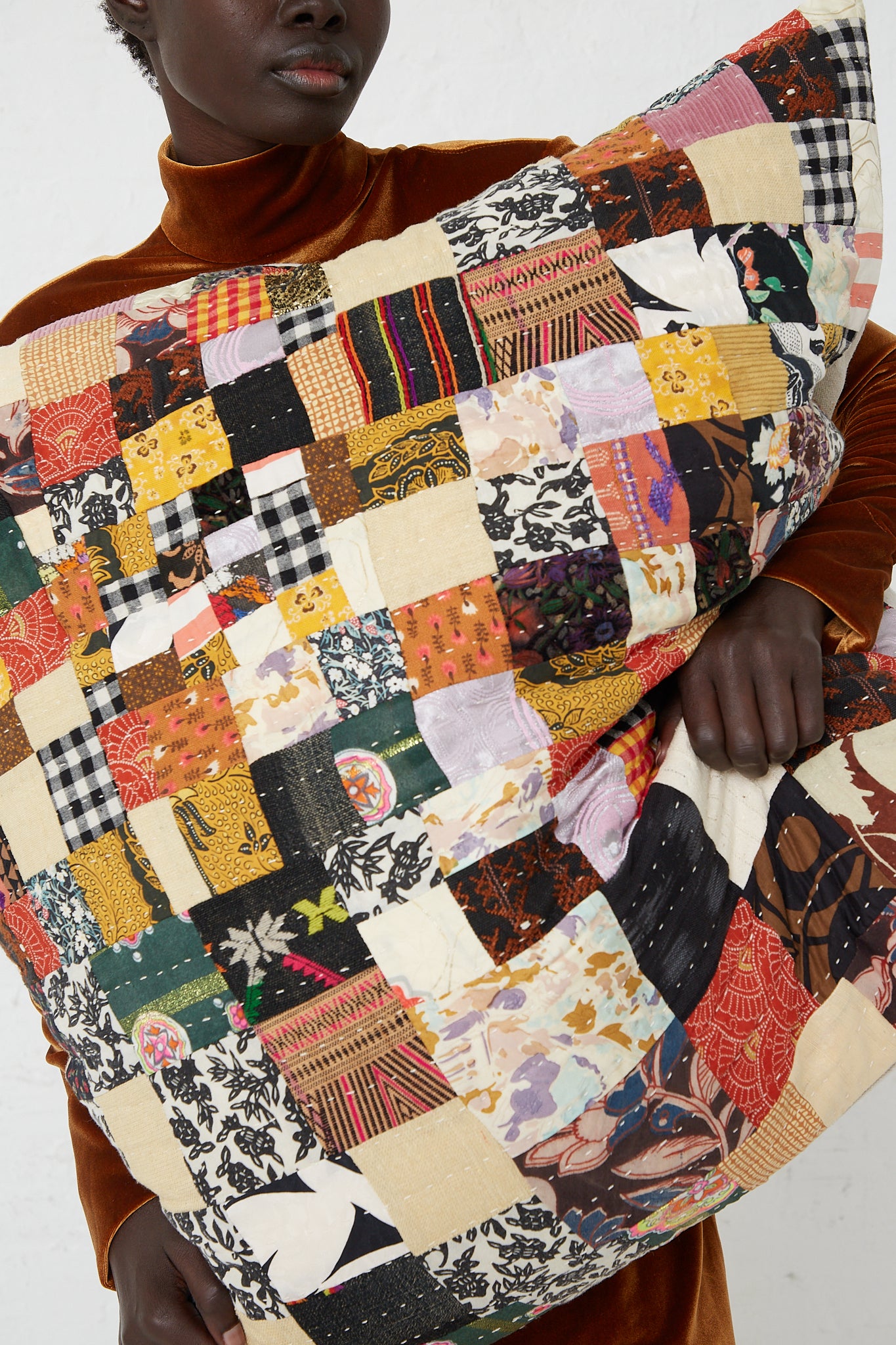 A woman is holding a Counterpane antique found cloth Patchwork Pillows in Brown Multi II.