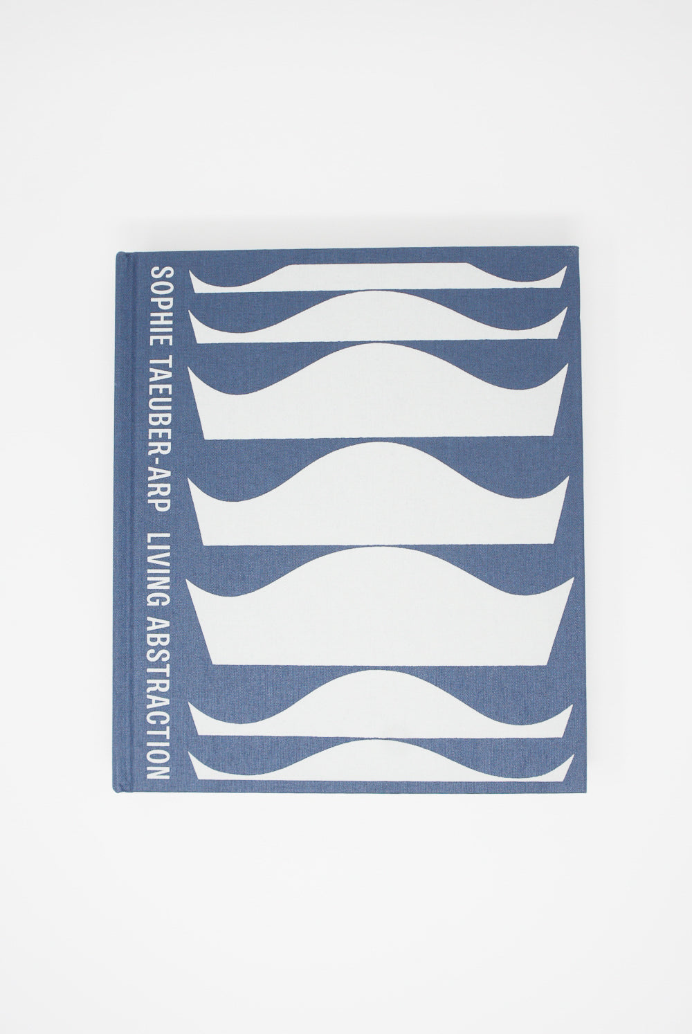A blue Sophie Taeuber-Arp: Living Abstraction book with white lines on it, showcasing a retrospective of Taeuber-Arp's abstract artistry by Artbook/D.A.P.