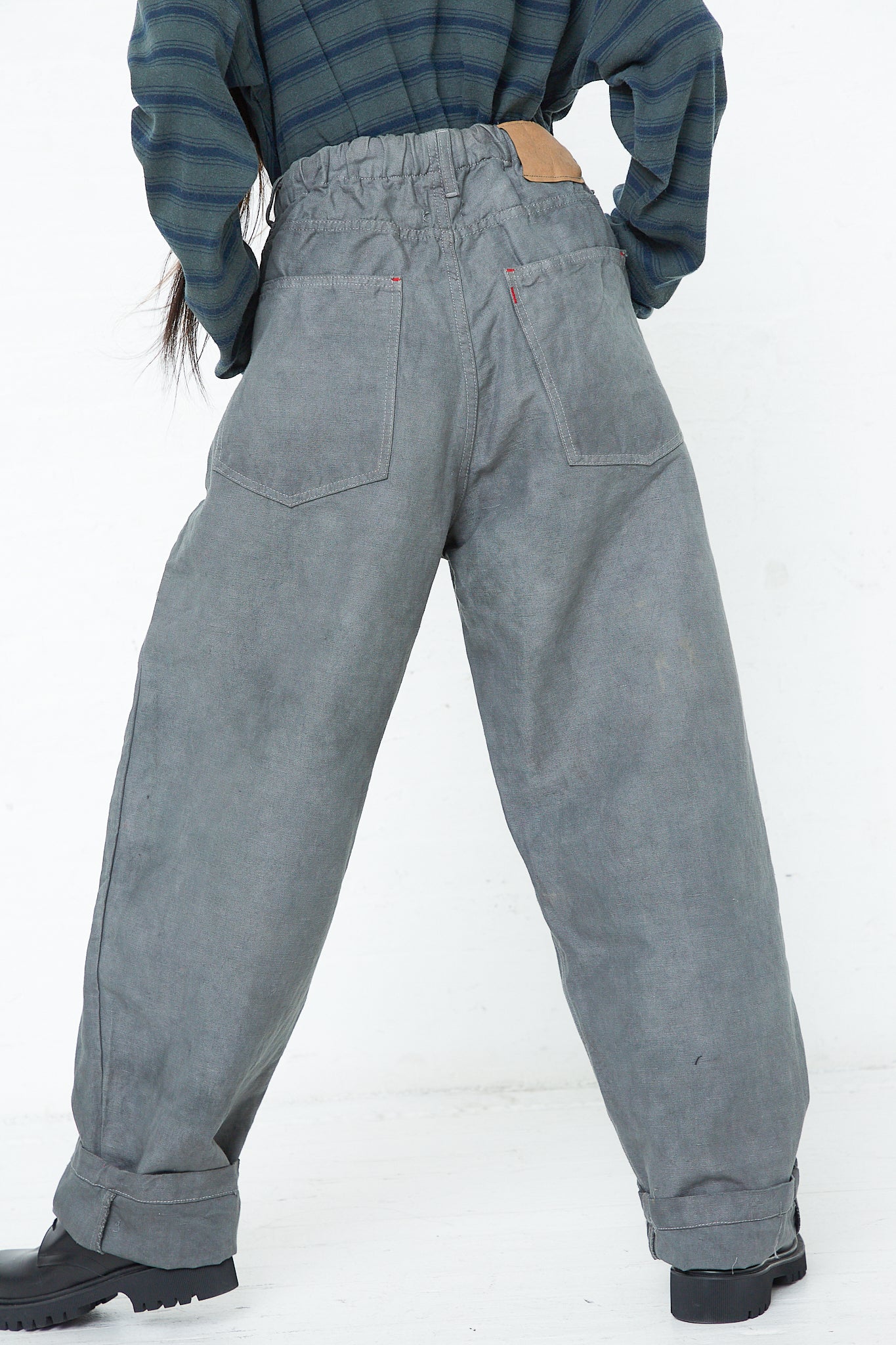 A woman is standing with her back to the camera in a pair of relaxed fit pants made from 9 oz. Cotton and Hemp P40 Z Boys Military Pant in Swiss Army by Dr. Collectors.