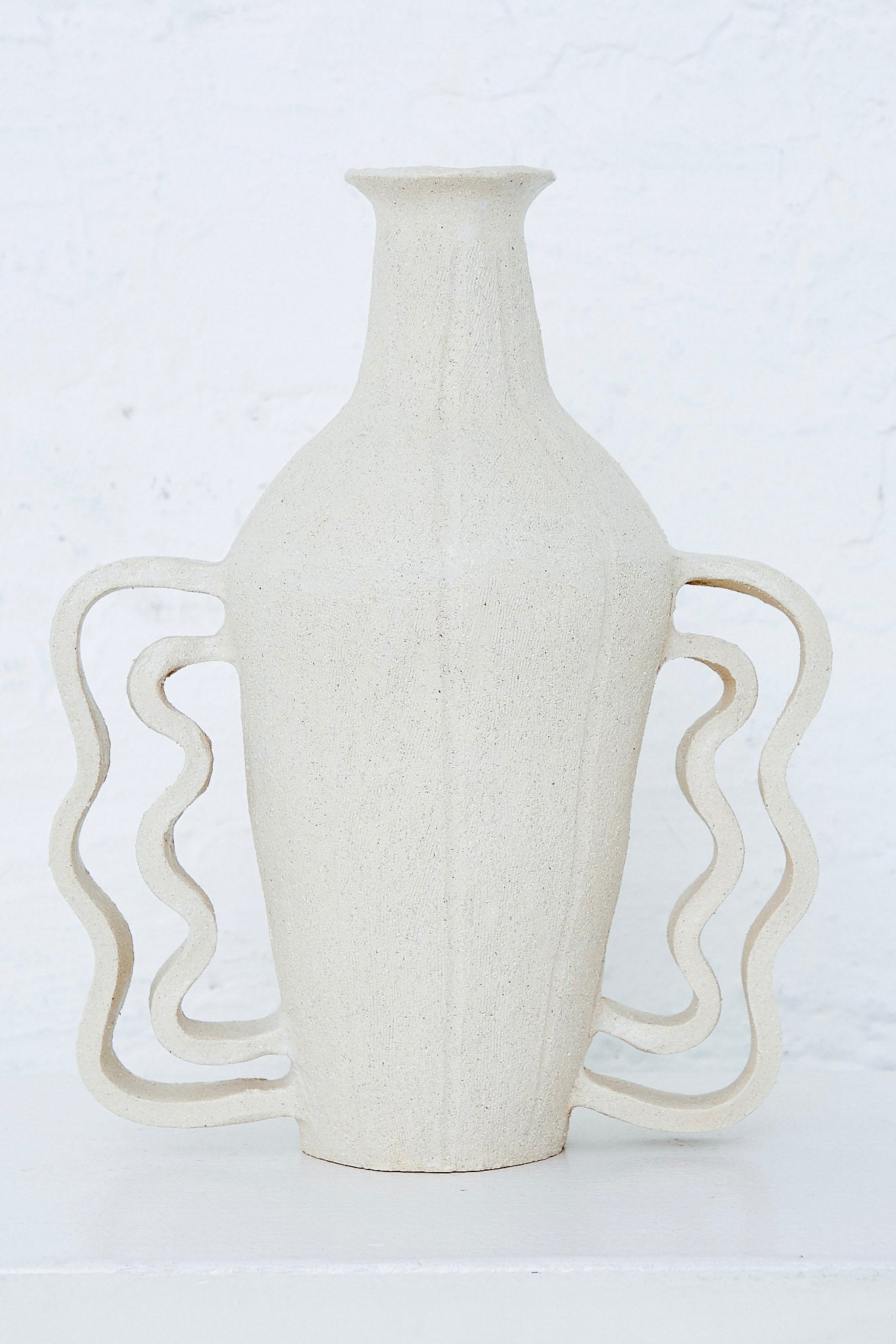 A Clandestine Amphora Le Grand Doubles Vagues white ceramic vase on a white table.