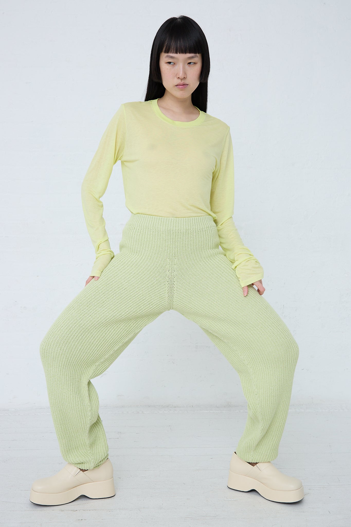 A woman in Baserange's Cotton Dodd Pant in Mimosa is posing in front of a white wall.