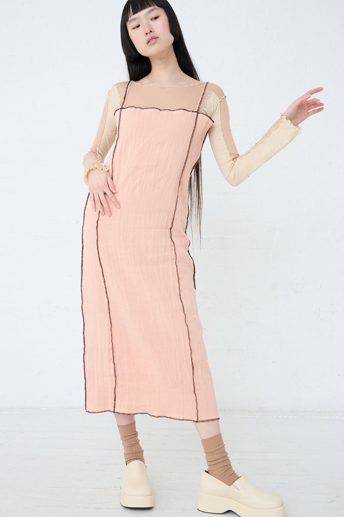 A woman wearing the Baserange Linen and Cotton Shok Slip Dress in Rose, paired with pink socks and white clogs. Front view and full length