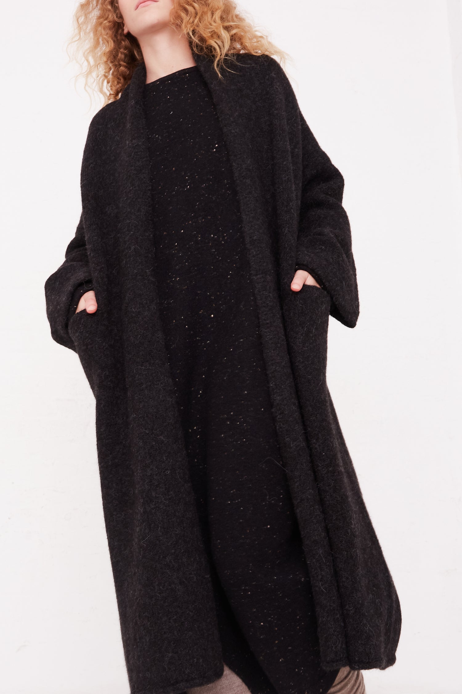 A woman wearing a black wool coat and Lauren Manoogian Long Shawl Cardigan in Black.