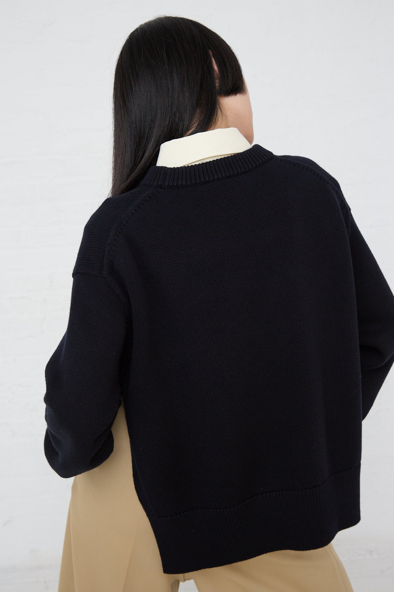 The back of a woman wearing a Studio Nicholson Merino Cotton Hima Side Split Crew Neck in Dark Navy with ribbed hem and cuffs.