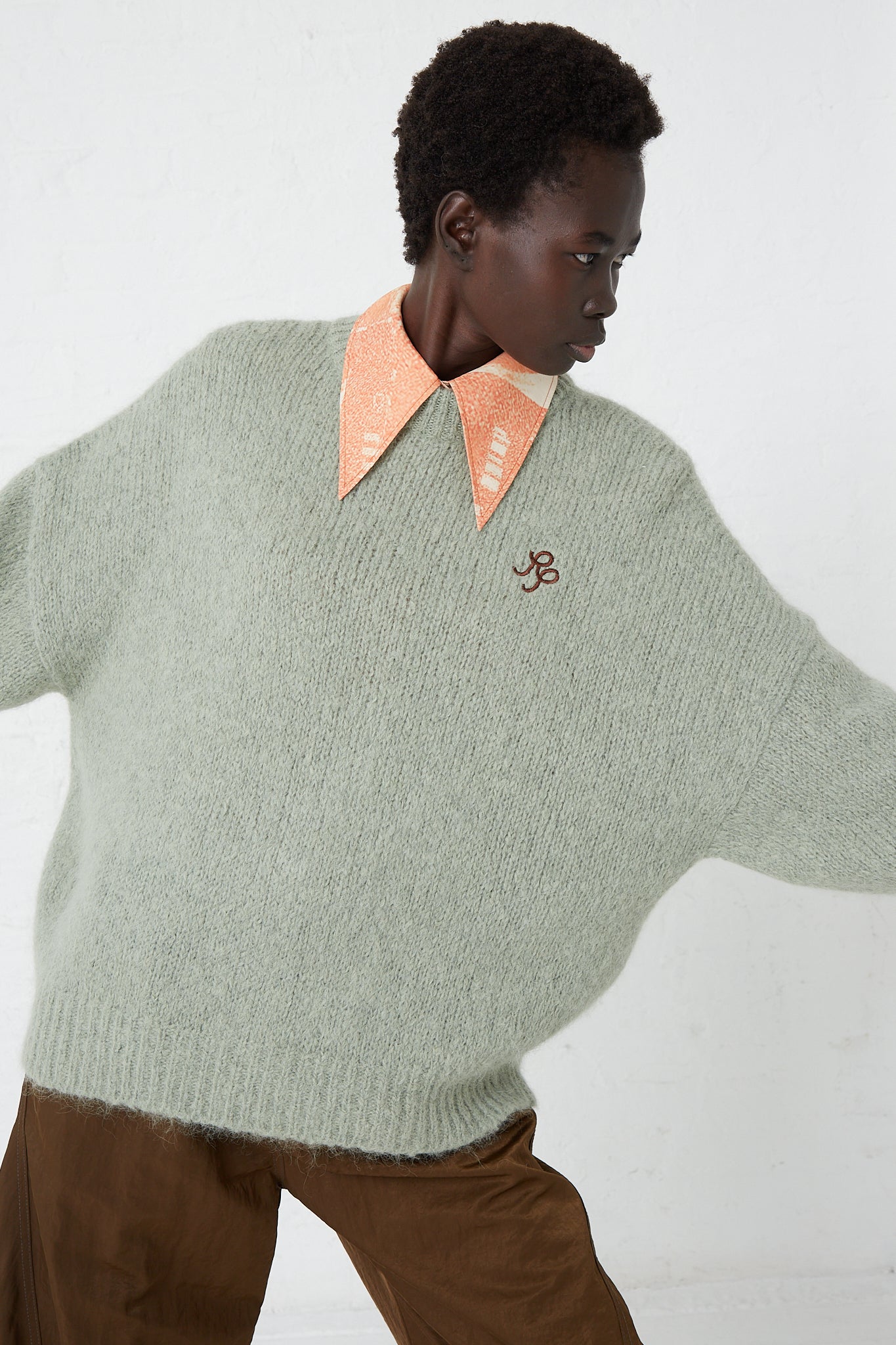 A woman donning a Rejina Pyo Alpaca Blend Toni Sweater in Mint, paired with brown pants.
