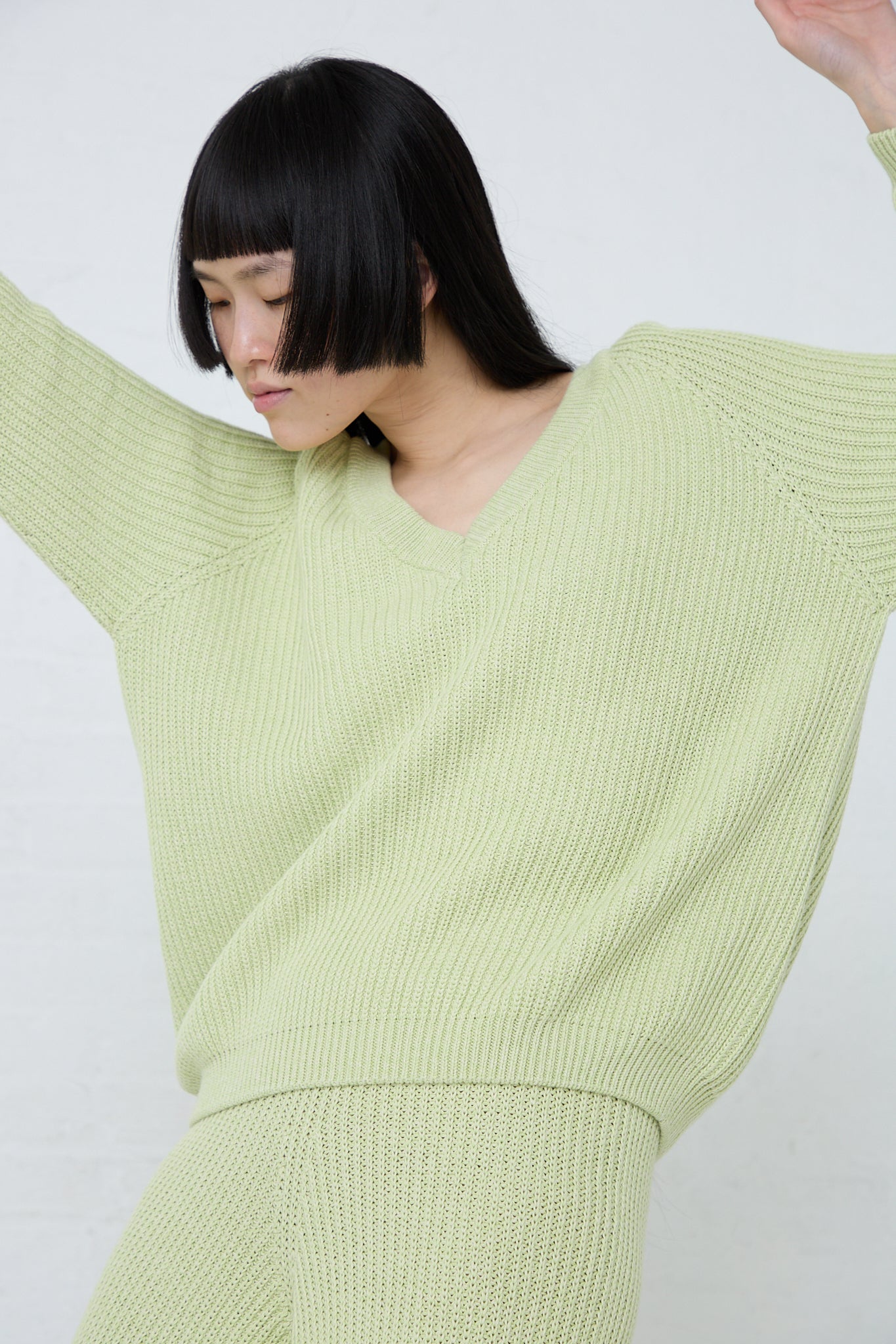 The model is wearing a slim fit cotton Dodd V Neck Pullover in Mimosa, made of ribbed organic cotton by Baserange. Side view.