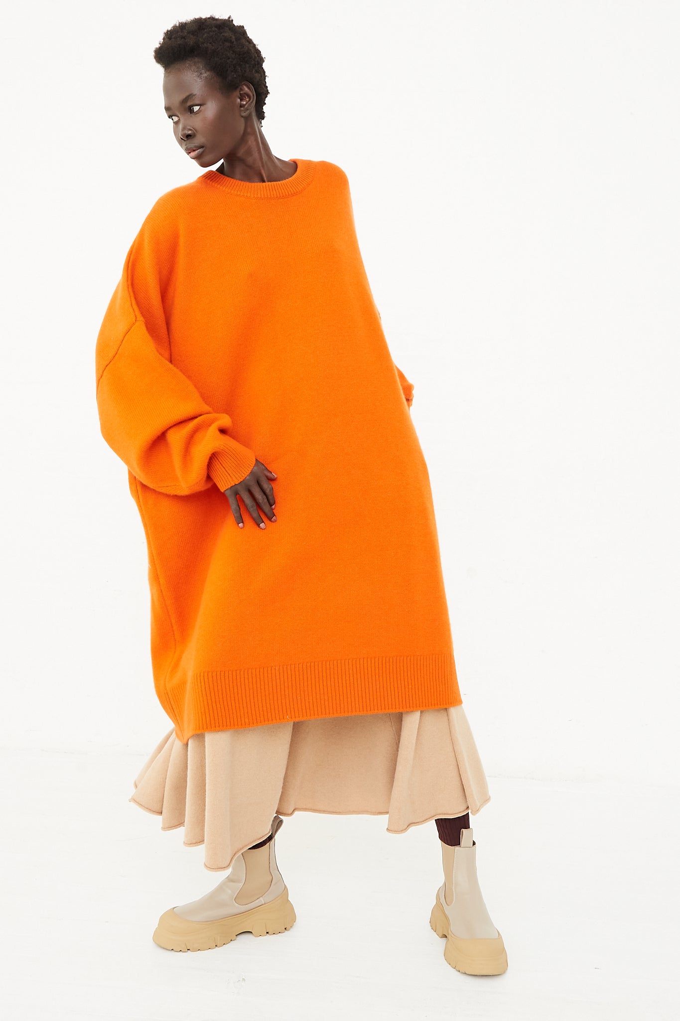 A model wearing the Extreme Cashmere No. 303 Sandra Dress in Maple posing in front of a white background at Oroboro store.