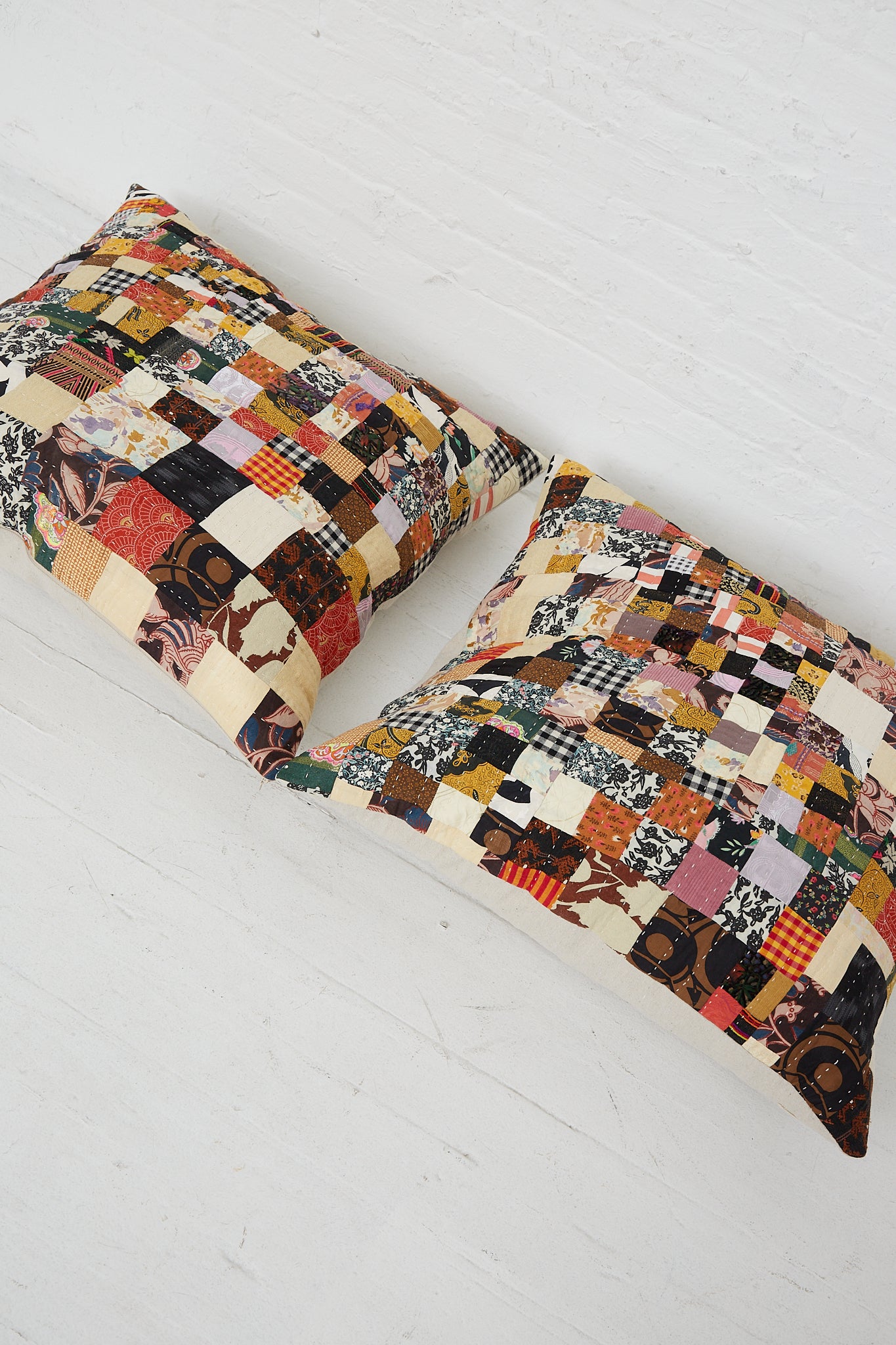 Two Counterpane Patchwork Pillows in Brown Multi II, with an antique found cloth design, displayed on a white floor.