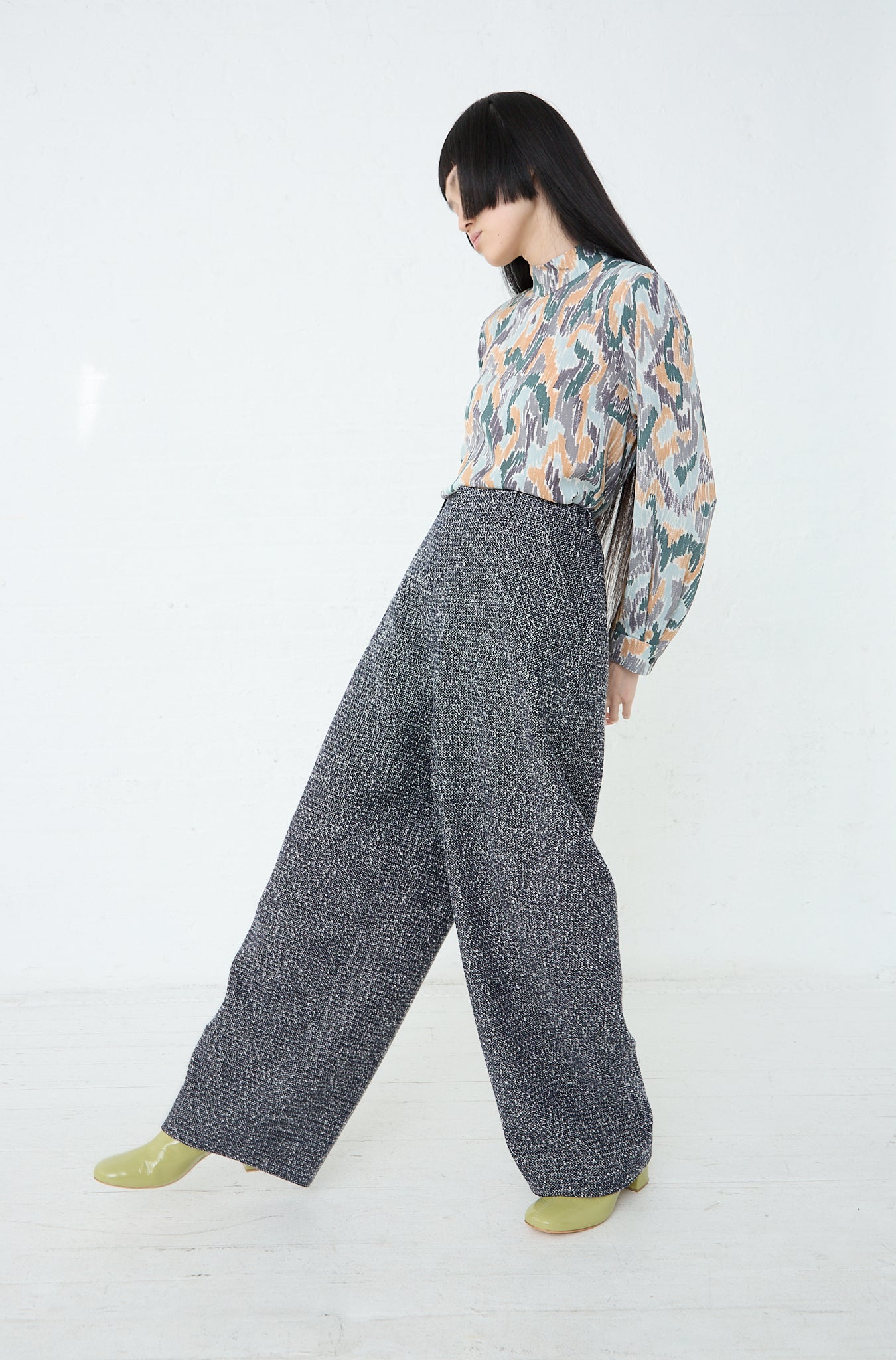 A woman wearing Predawn Trousers in Navy Mix made by Mina Perhonen and a blouse with relaxed fit. Side view and full length.