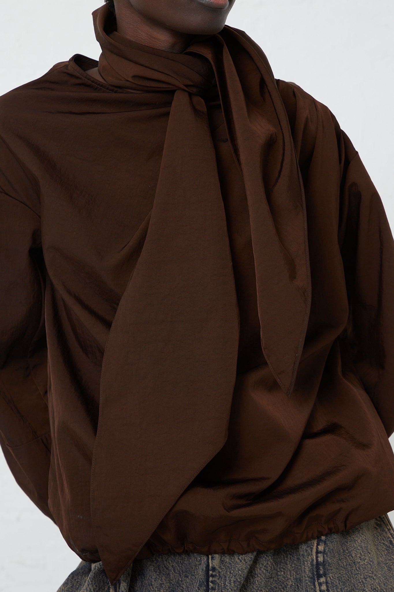 A woman wearing a brown shirt and jeans, sporting the Veronique Leroy Zipped on Sleeve Rain Blouse in Choco, made of taffeta nylon.