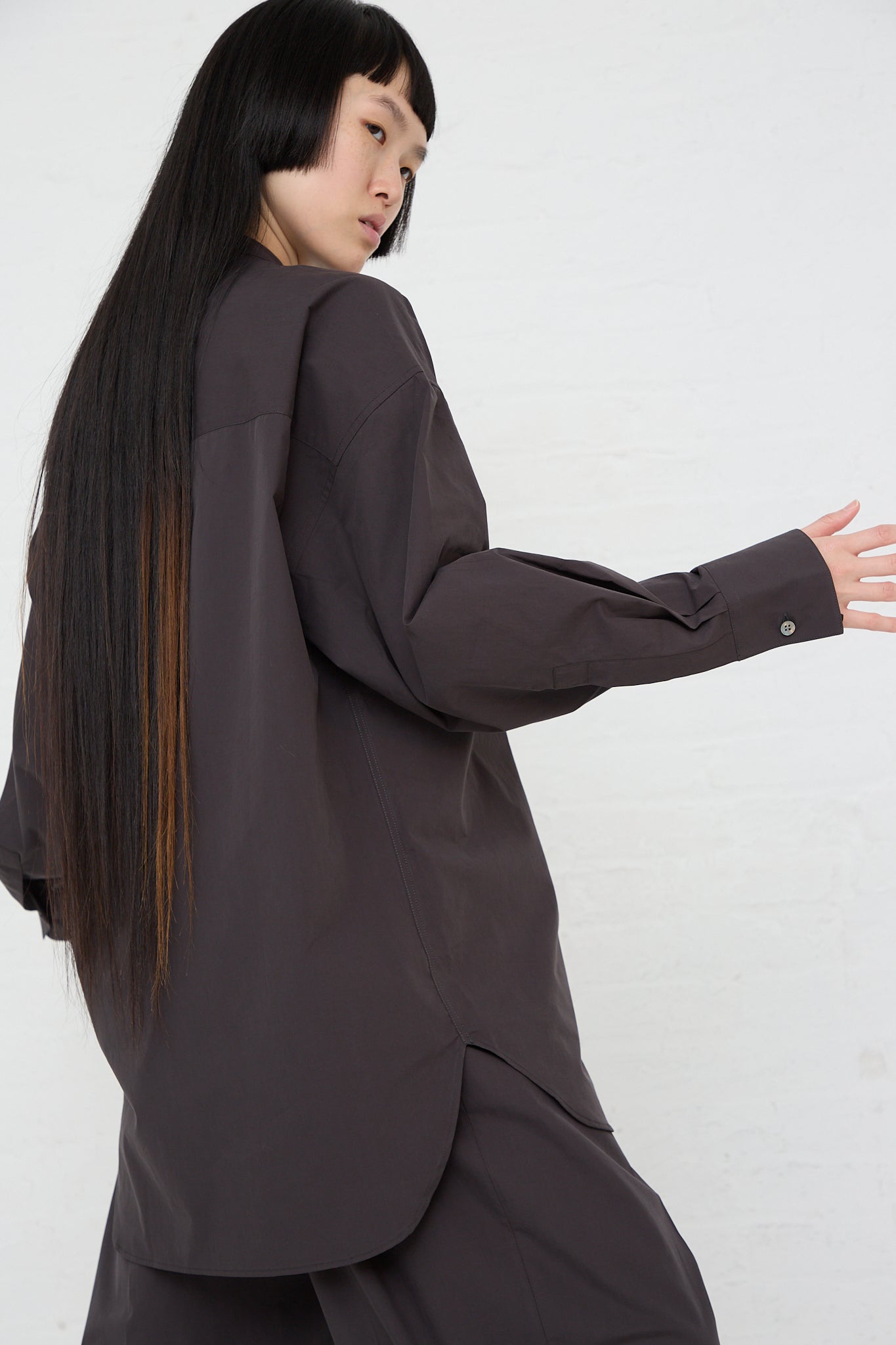 A woman wearing a Frink Half Placket Shirt in Asphalt by Studio Nicholson. Side view.