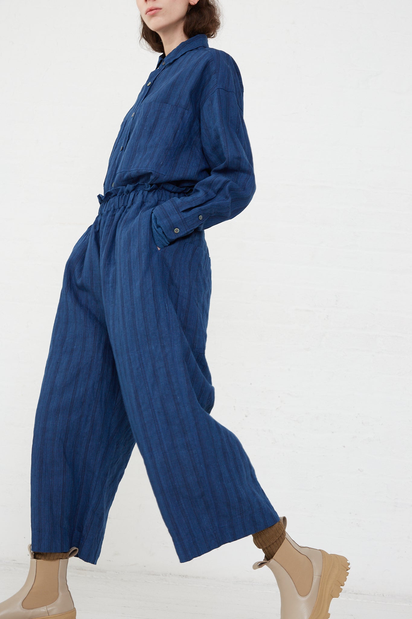 A woman wearing the Ichi Antiquités Woven Linen Pant in Indigo Stripes jumpsuit and boots, featuring an elasticated waist for comfort.