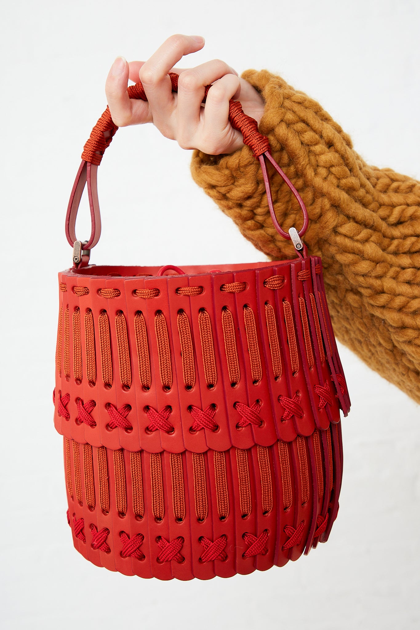 A person holding a Hatori Bucket Bag 80 in Amaranto, Cherry and Tangerine with an adjustable strap.