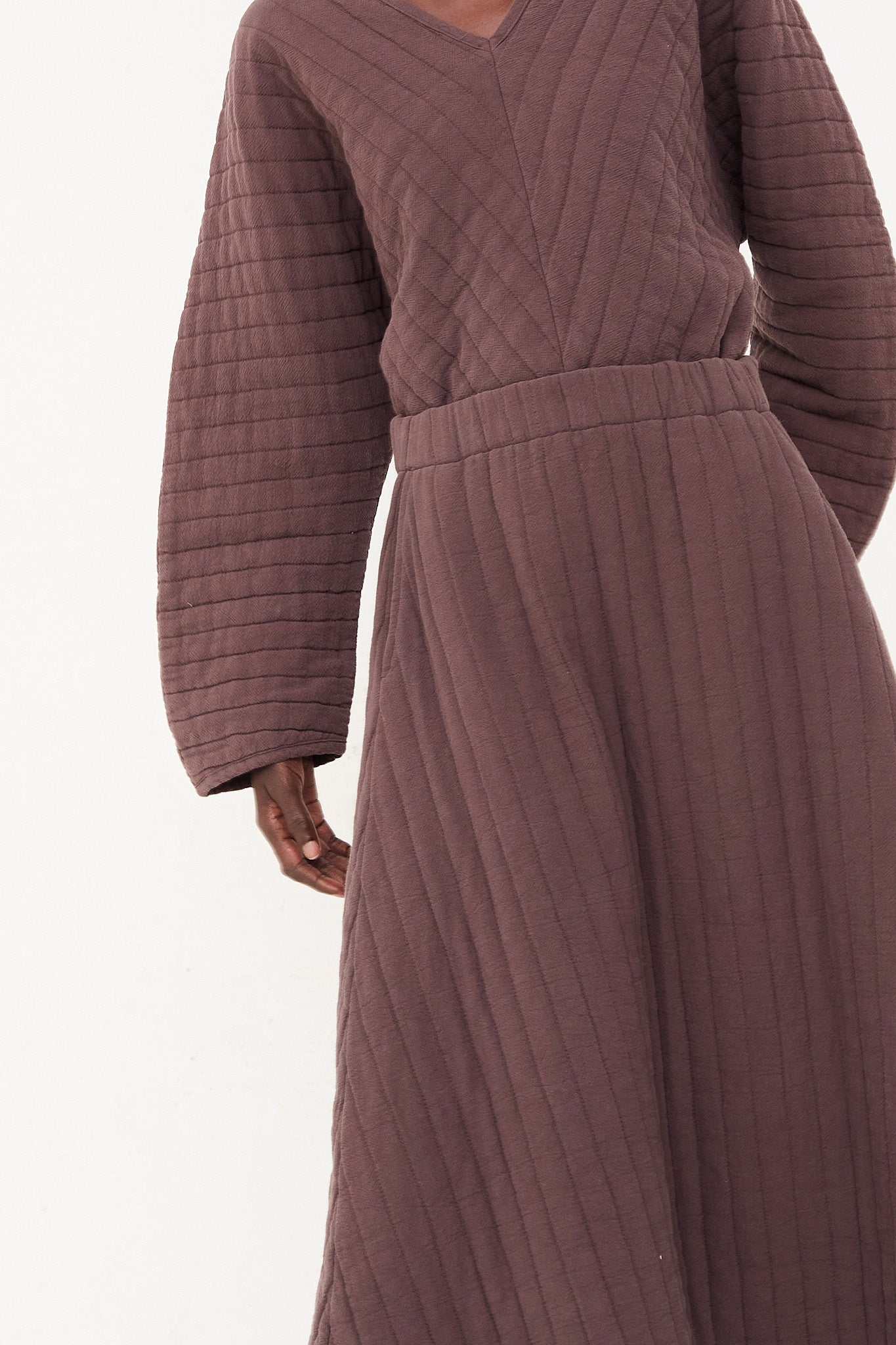 The model is wearing a plum quilted skirt with an elasticated waist, from Black Crane.
