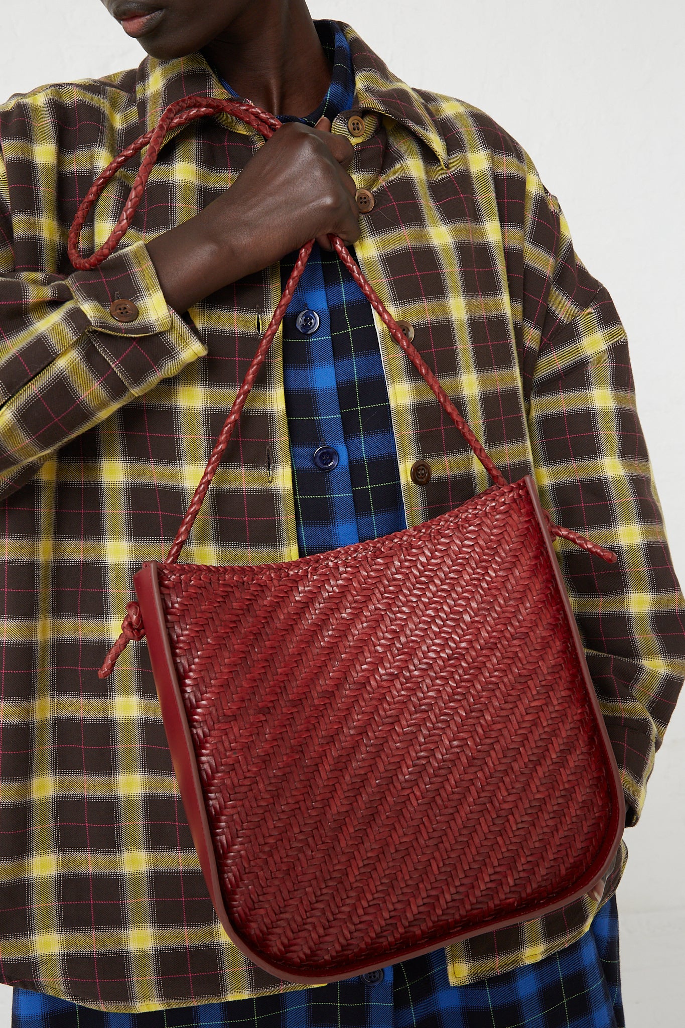 A woman in a plaid shirt is holding a Dragon Diffusion Wanaka Crossbody Bag in Bordo. Available at Oroboro Store.
