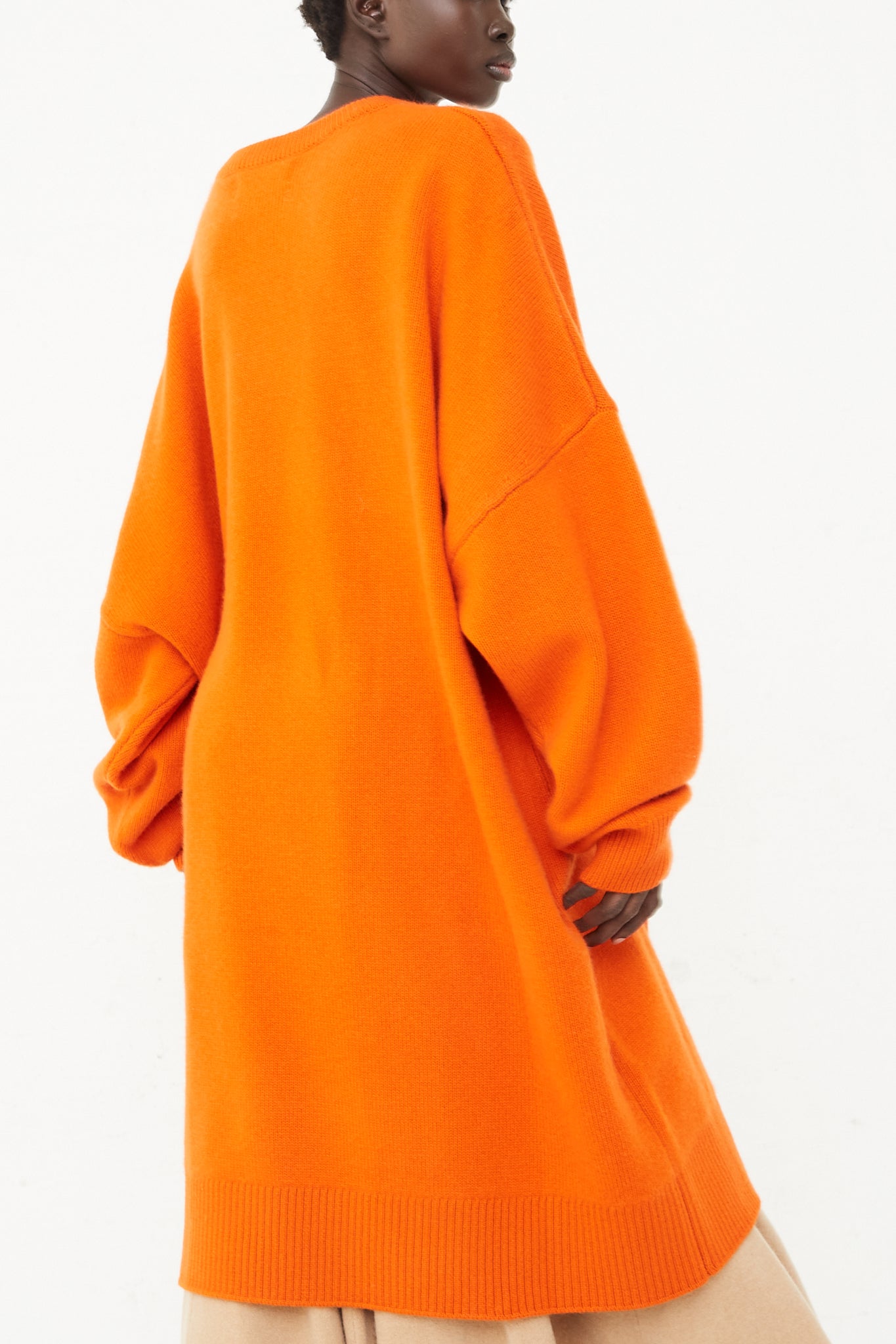 The back view of a model wearing an orange long-sleeved sweater from the Extreme Cashmere collection at Oroboro Store.