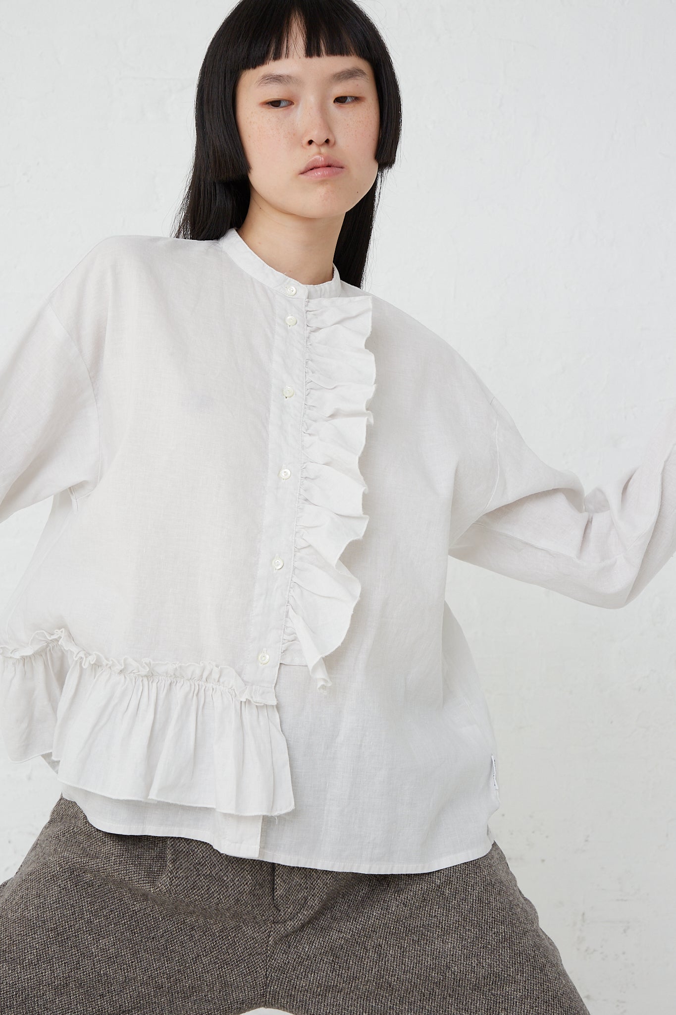 The model is wearing a nest Robe UpcycleLino Linen Gathered Frill Blouse in Off White with ruffles made from an upcycled linen and cotton blend.