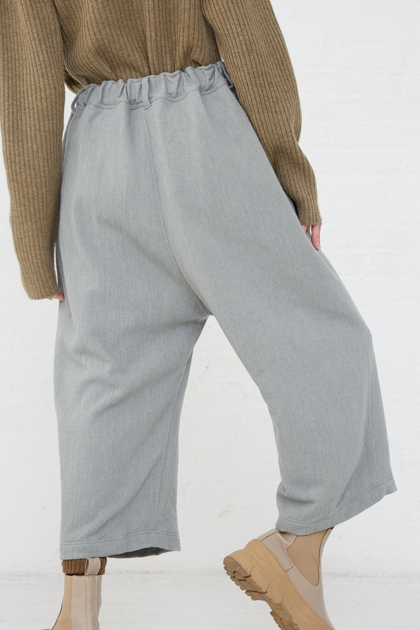 The back view of a woman wearing an Ichi Antiquités Merino Wool Orihimedaki Pant in Blue with an elasticated waist, rendered in a chic grey color.