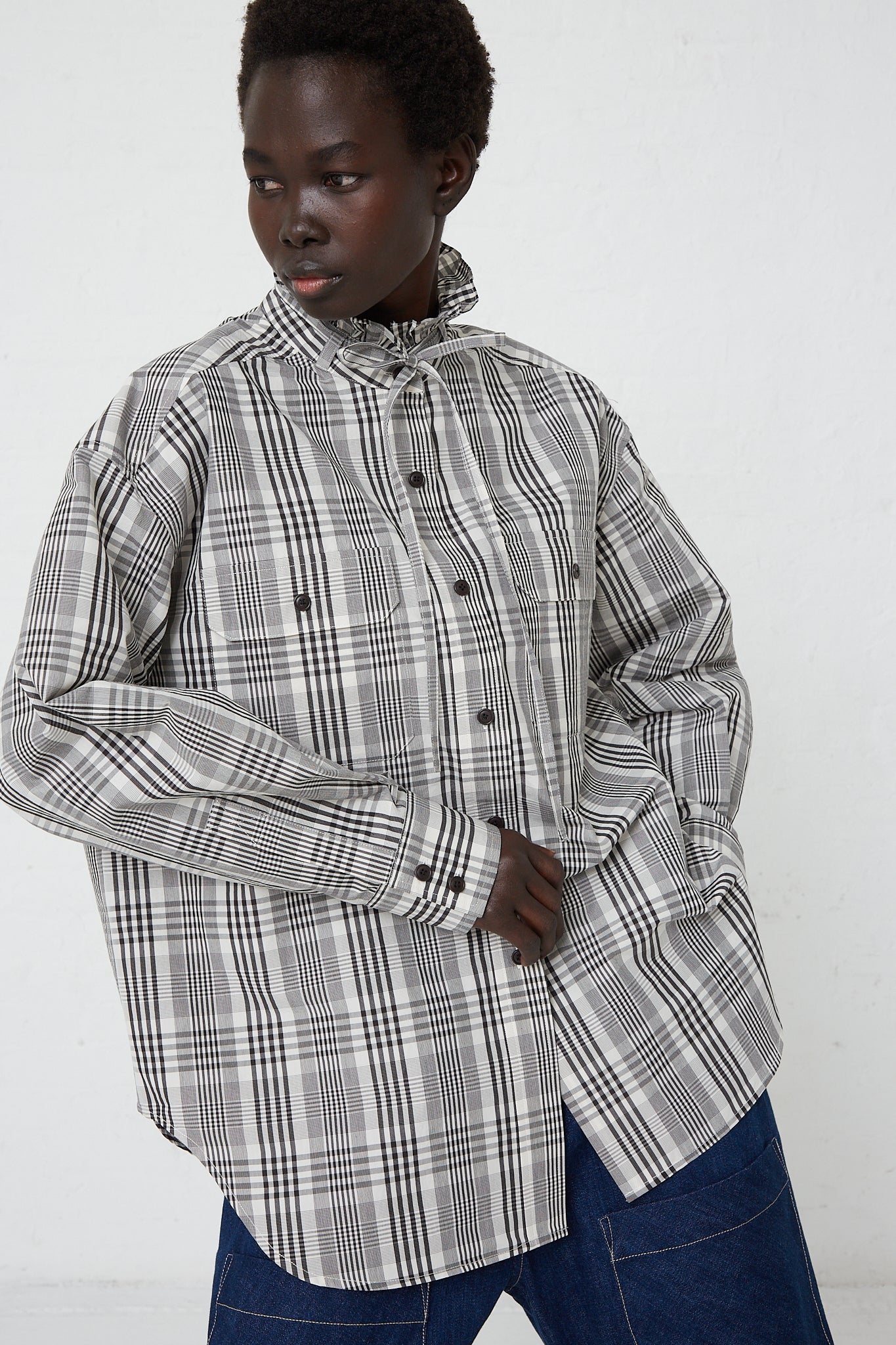A woman wearing a KasMaria Poplin Tie Shirt with Ruffle Collar in Heavy Plaid and jeans.