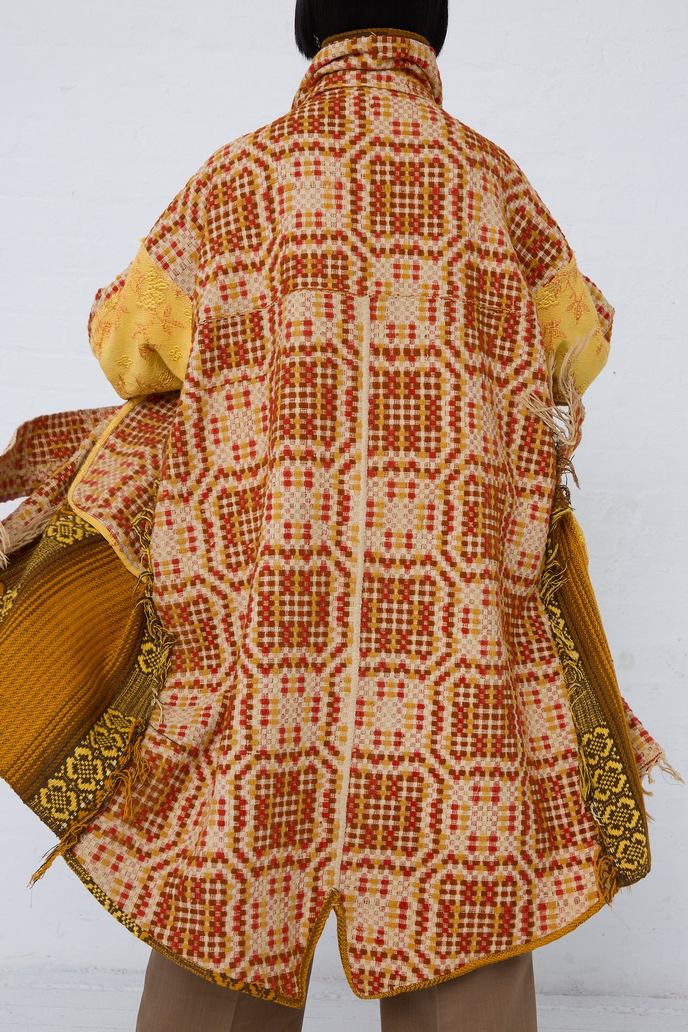 A woman wearing a Thank You Have A Good Day Patchwork Blanket Scarf Parka in Red, Yellow and Brown. Back view. 